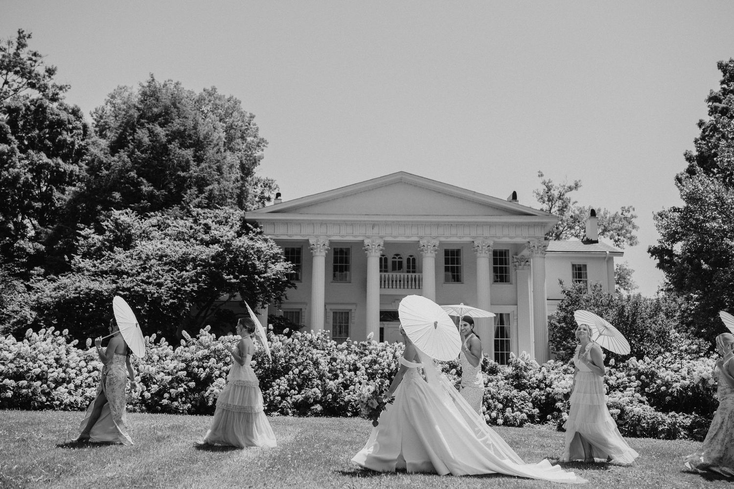 A sequence of six vintage black and white photos showing people in flowing white dresses walking near a classical building.
