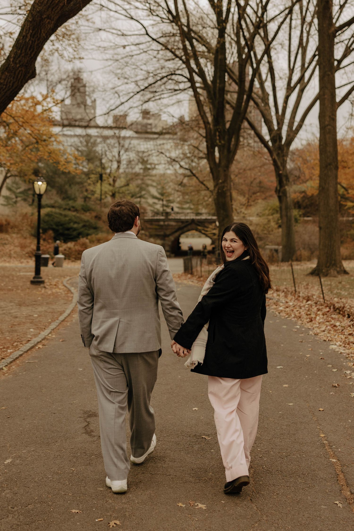 A couple walks together on a leaf-covered path in a park during autumn, captured in a warm sepia tone.