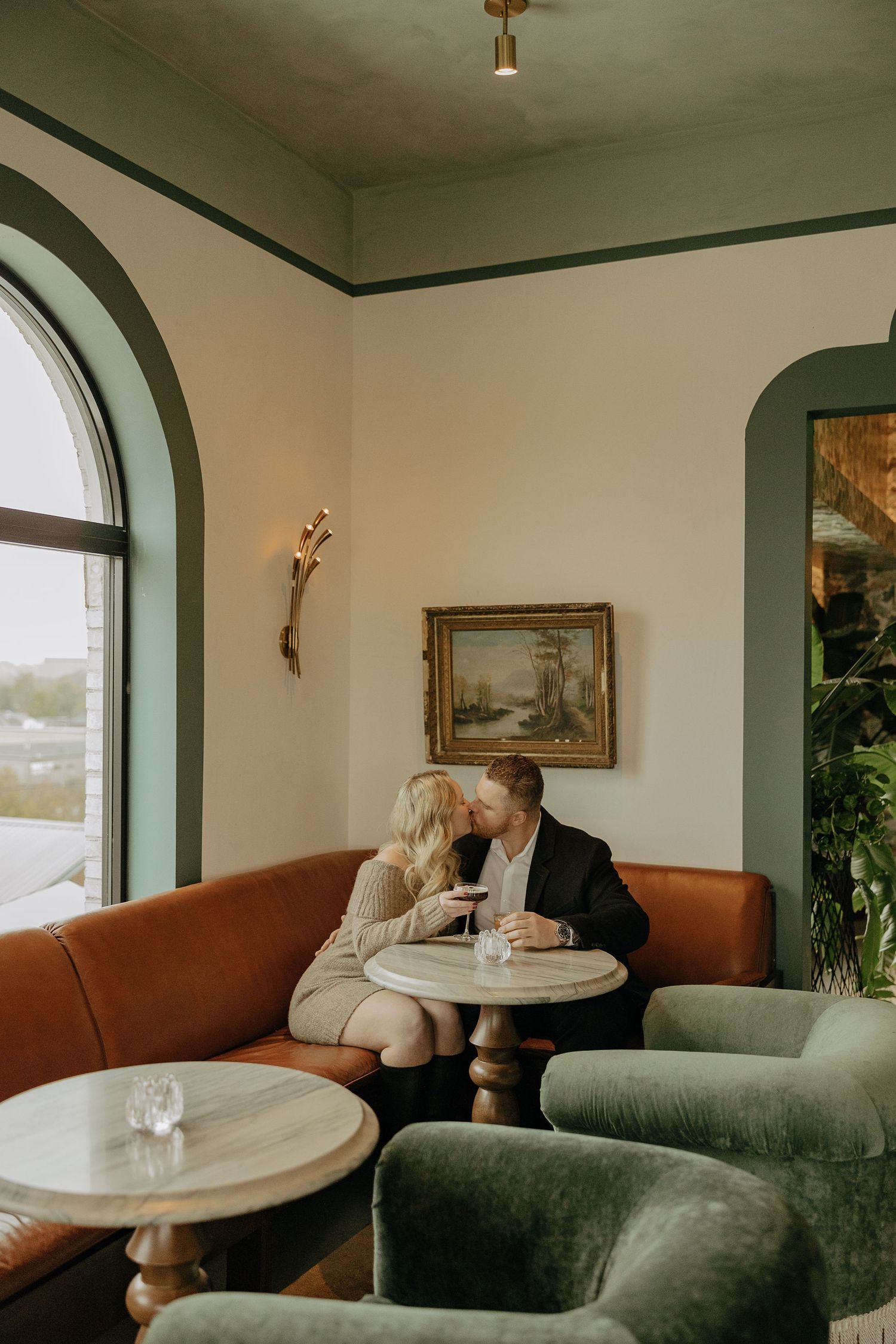 A romantic couple sits together in a cozy restaurant booth with arched windows and vintage decor.