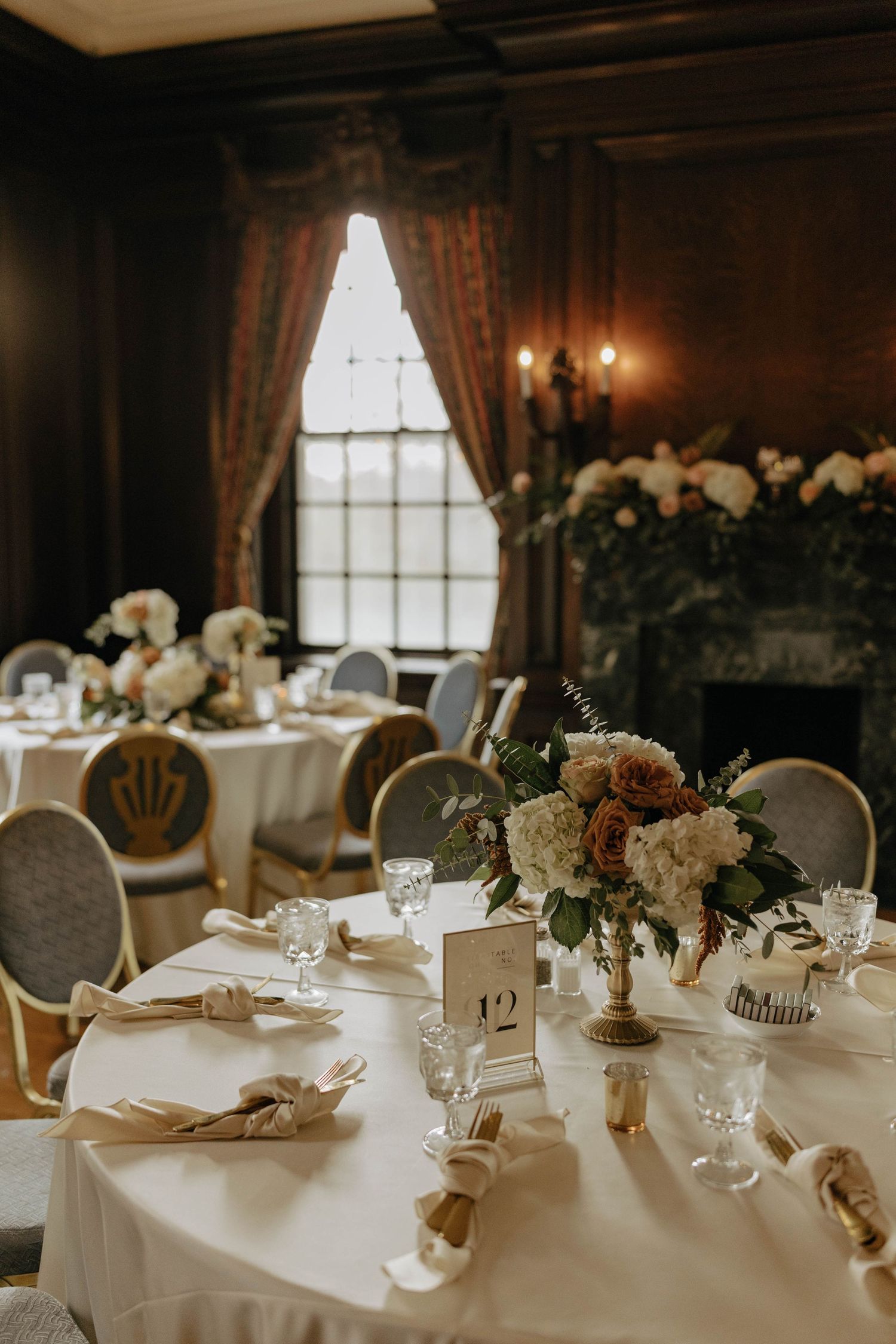 Elegant wedding reception tables set with white linens, floral centerpieces and glowing candles in a rustic wooden venue.
