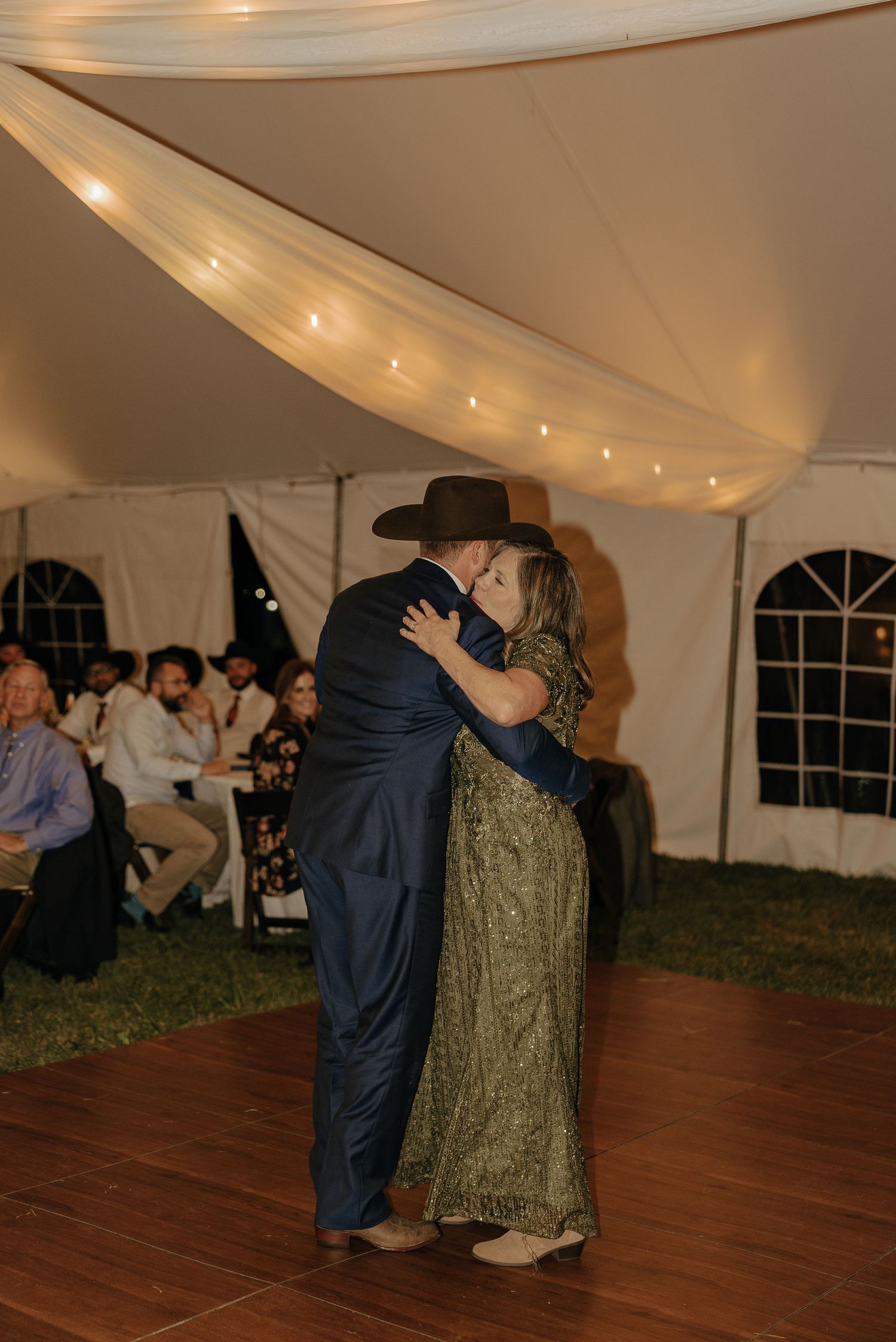 Couples dance under a white tent with string lights during an evening wedding reception.
