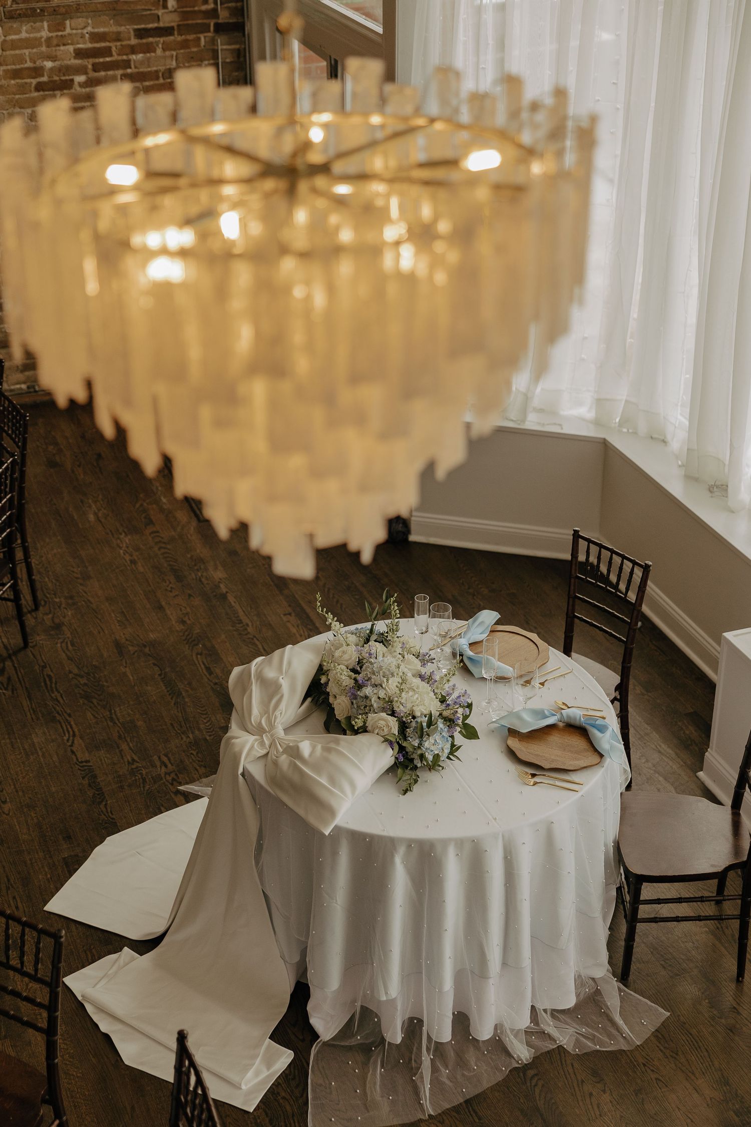 Elegant wedding reception tables with white linens and chandeliers in rustic venue.
