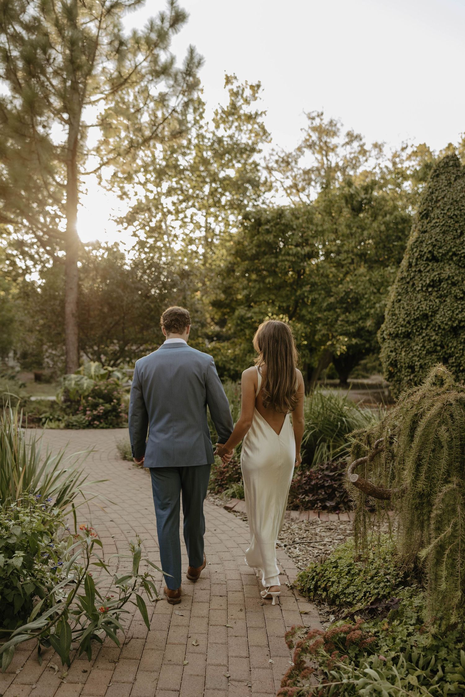 Newlyweds walking hand in hand down a garden path during golden hour.