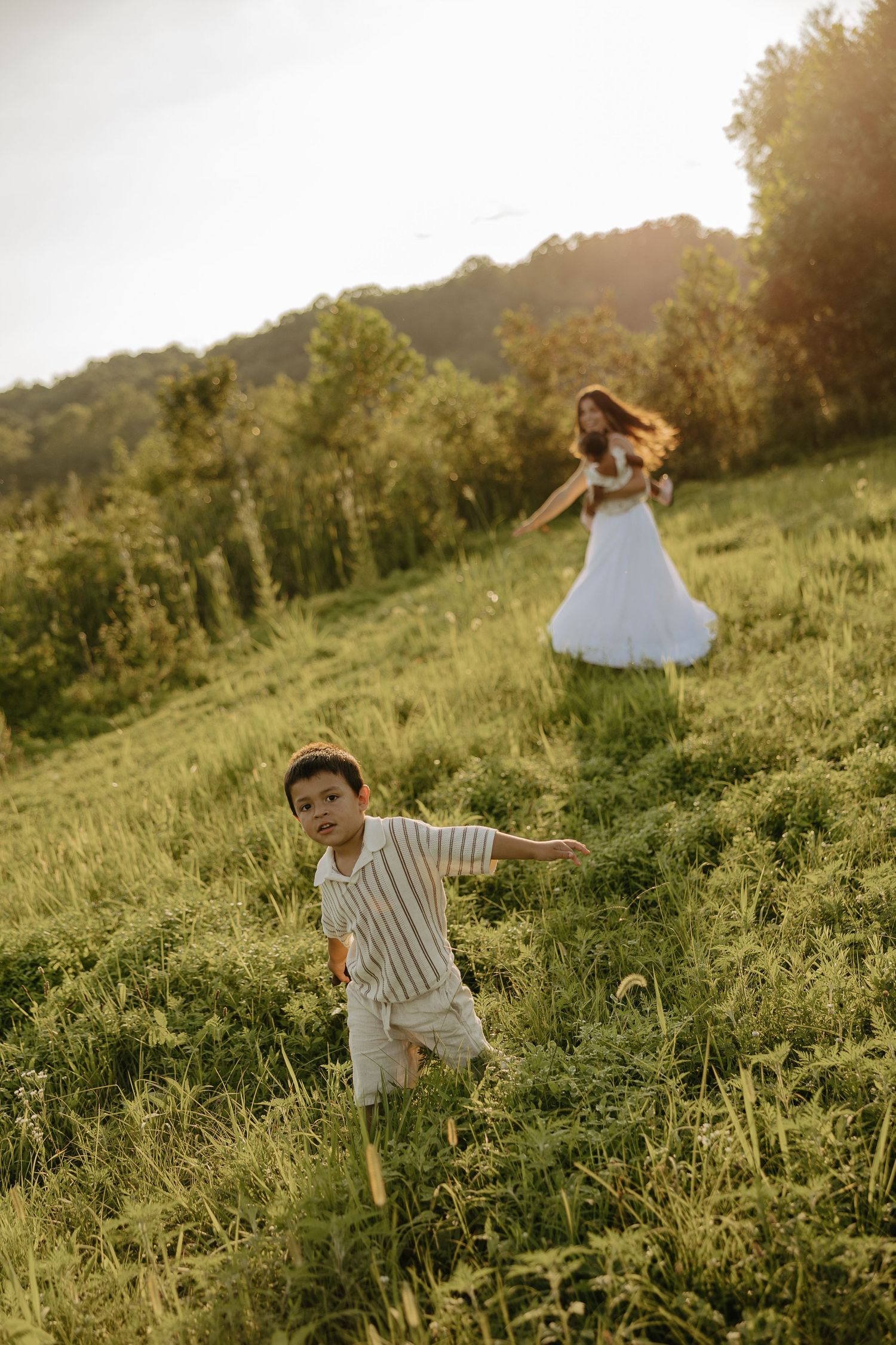 Playful moments captured in a sun-drenched field during family photoshoot.