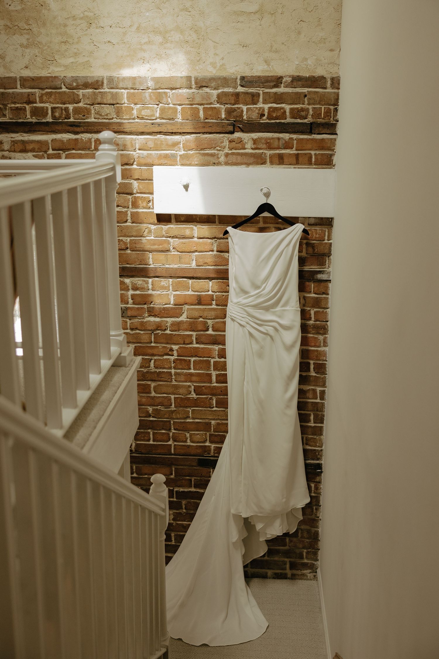 A series of photos showing a white wedding dress hanging against exposed brick walls in different angles.