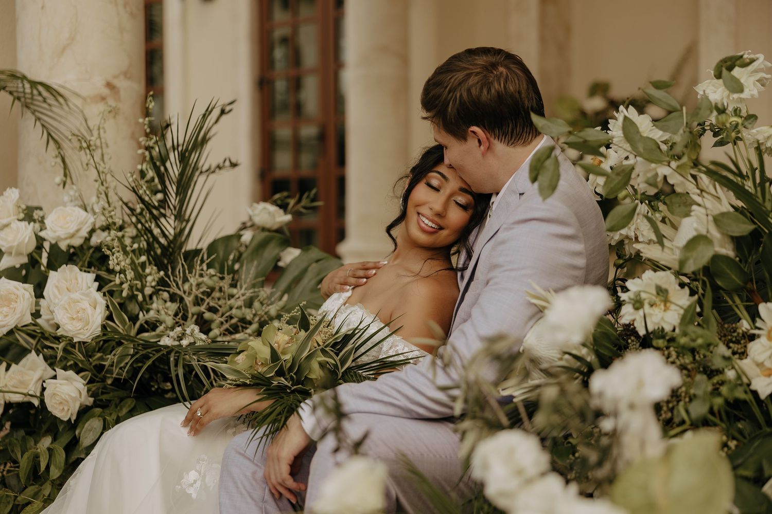 A romantic wedding scene with delicate white floral arrangements and greenery framing an intimate moment.