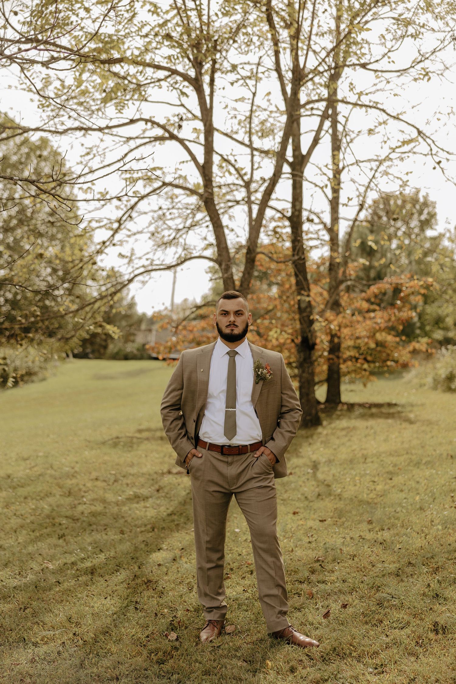 Autumn outdoor portrait showing tan suit against a natural hillside backdrop.
