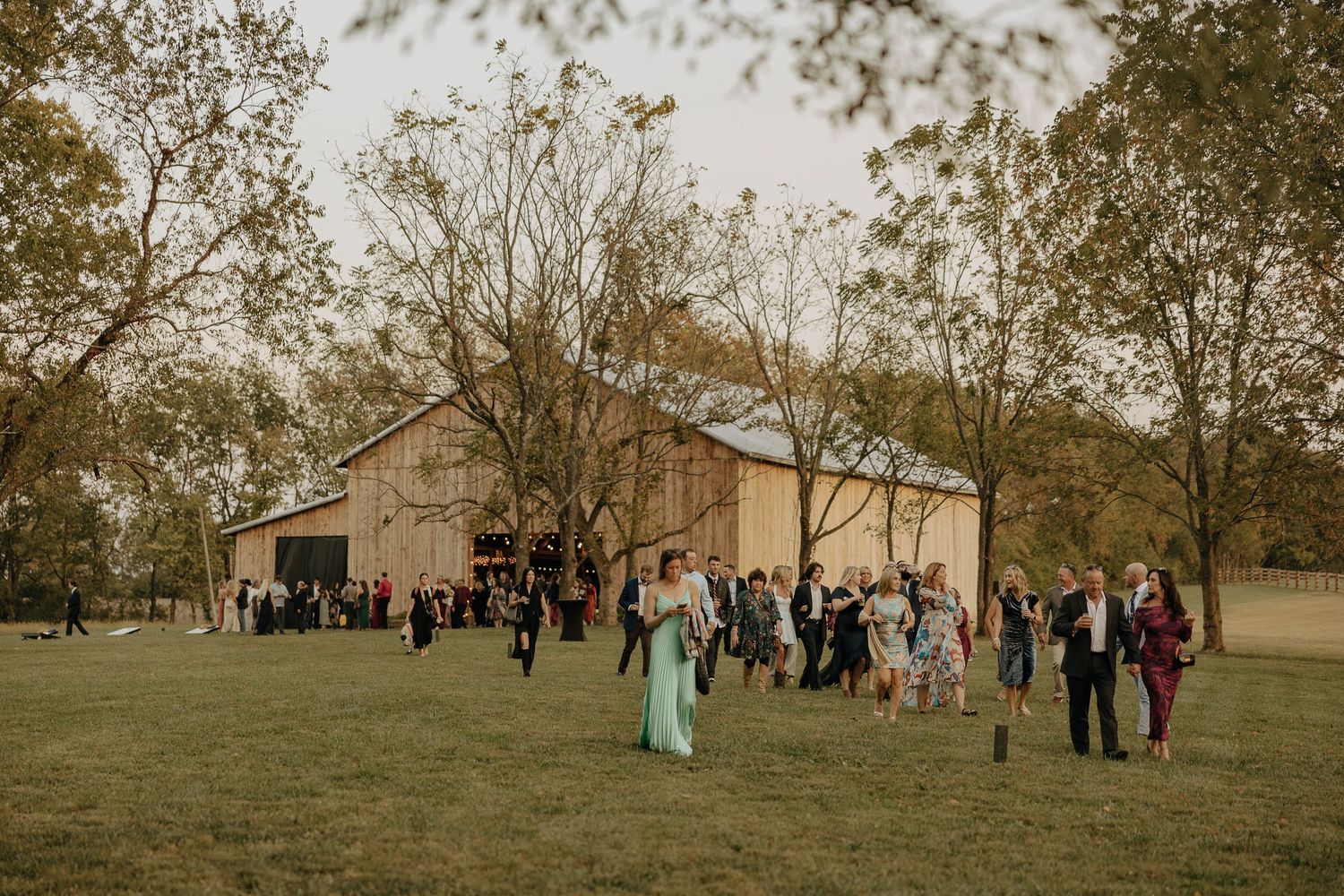 Wedding guests gather on a grassy hill during an outdoor autumn ceremony.