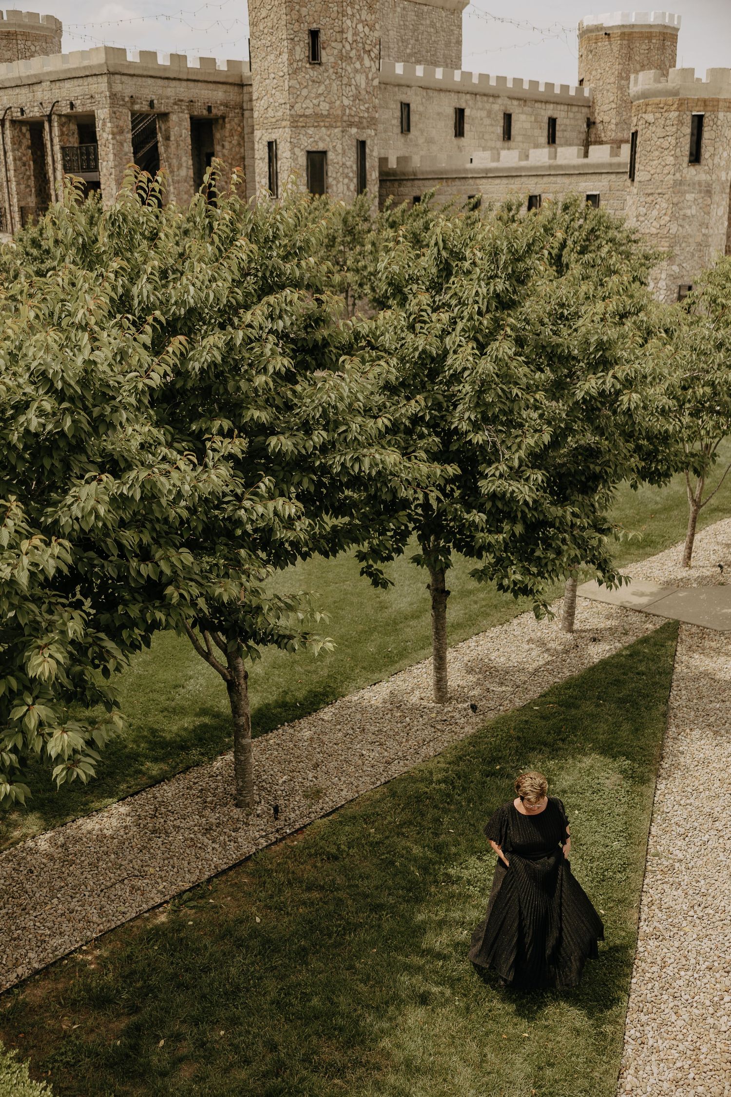 A dramatic aerial view of castle grounds with stone walls and manicured trees.