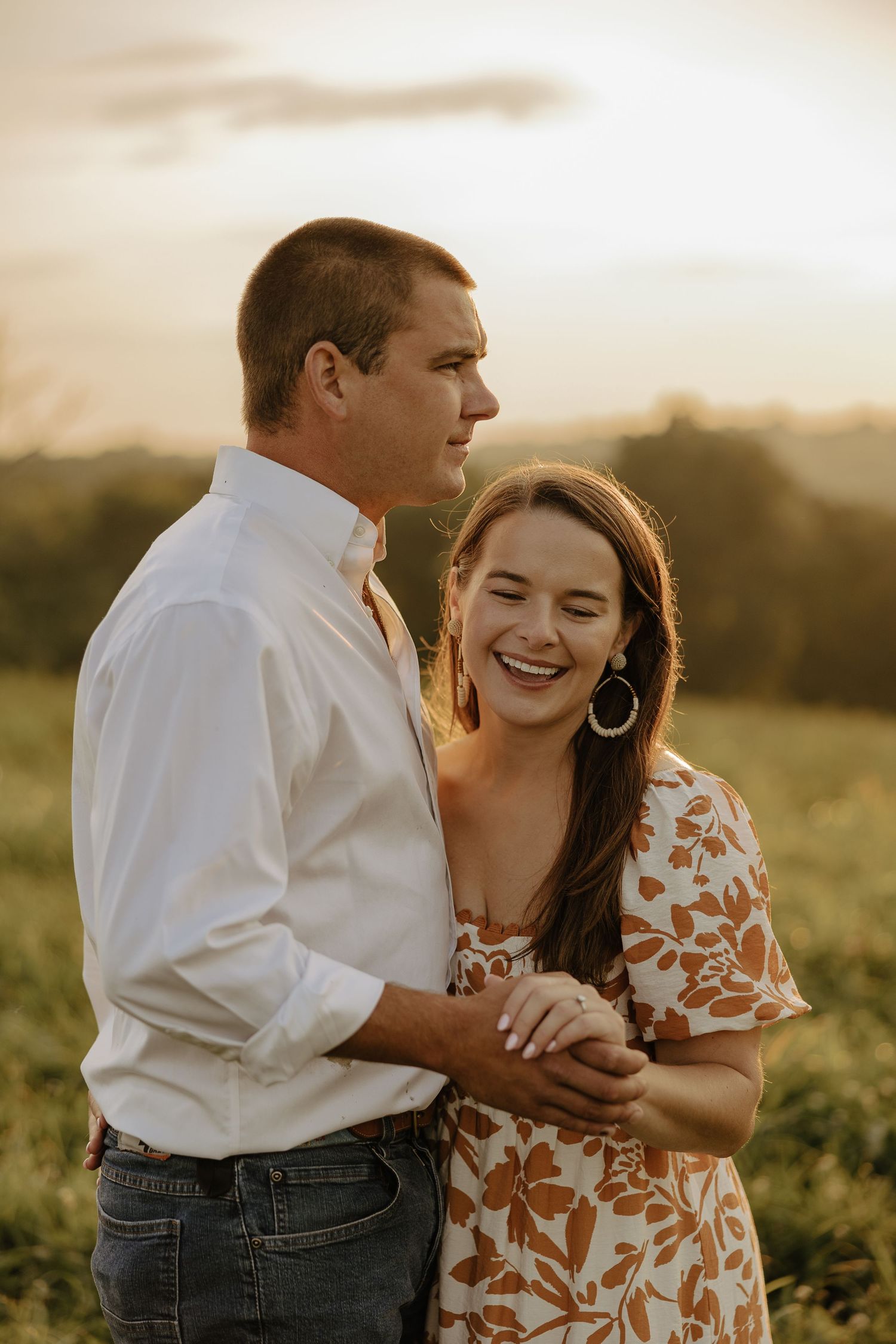 A couple shares laughter together in a sunlit field during their engagement photoshoot.