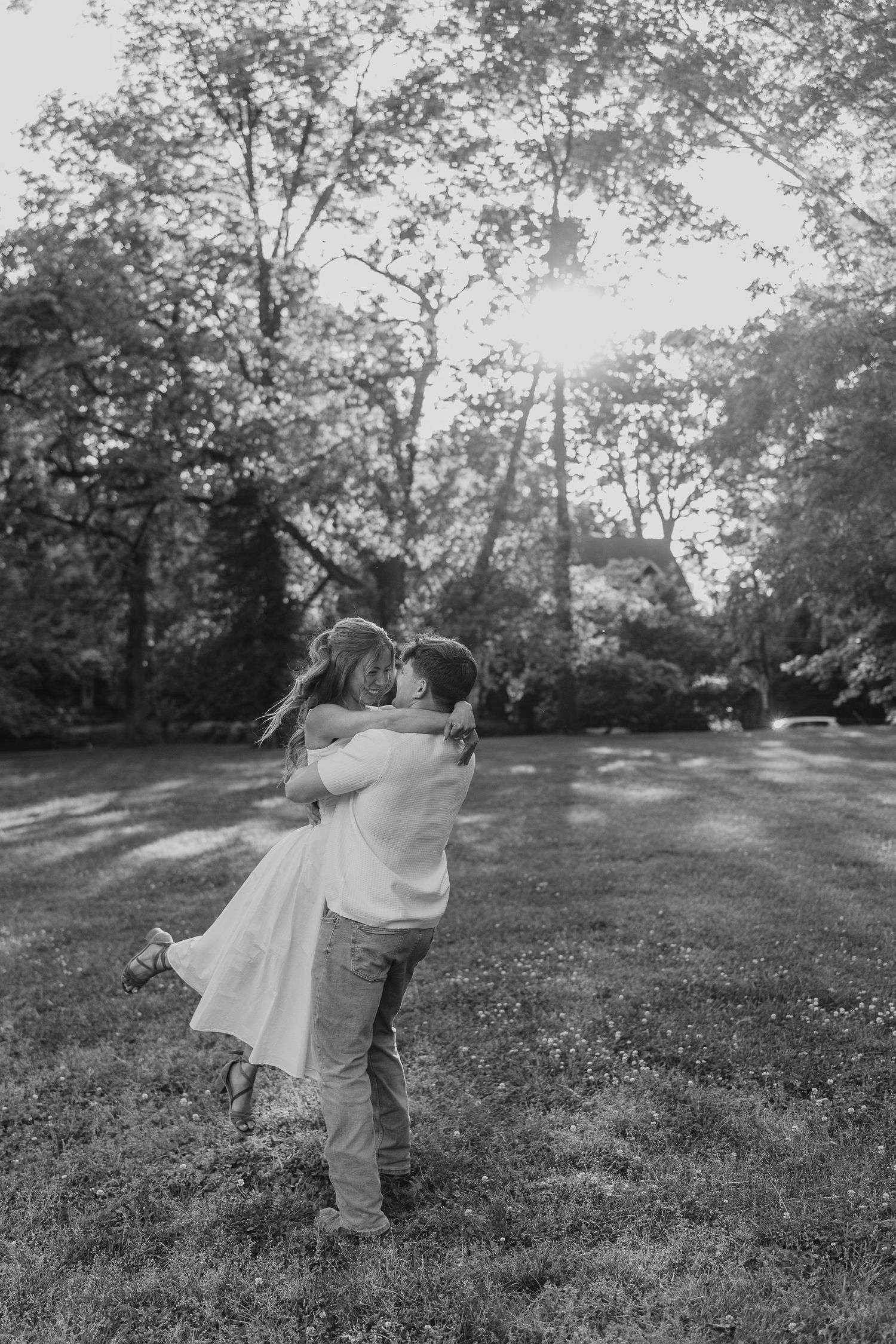 Black and white photo of a couple embracing and kissing in a sunlit park.