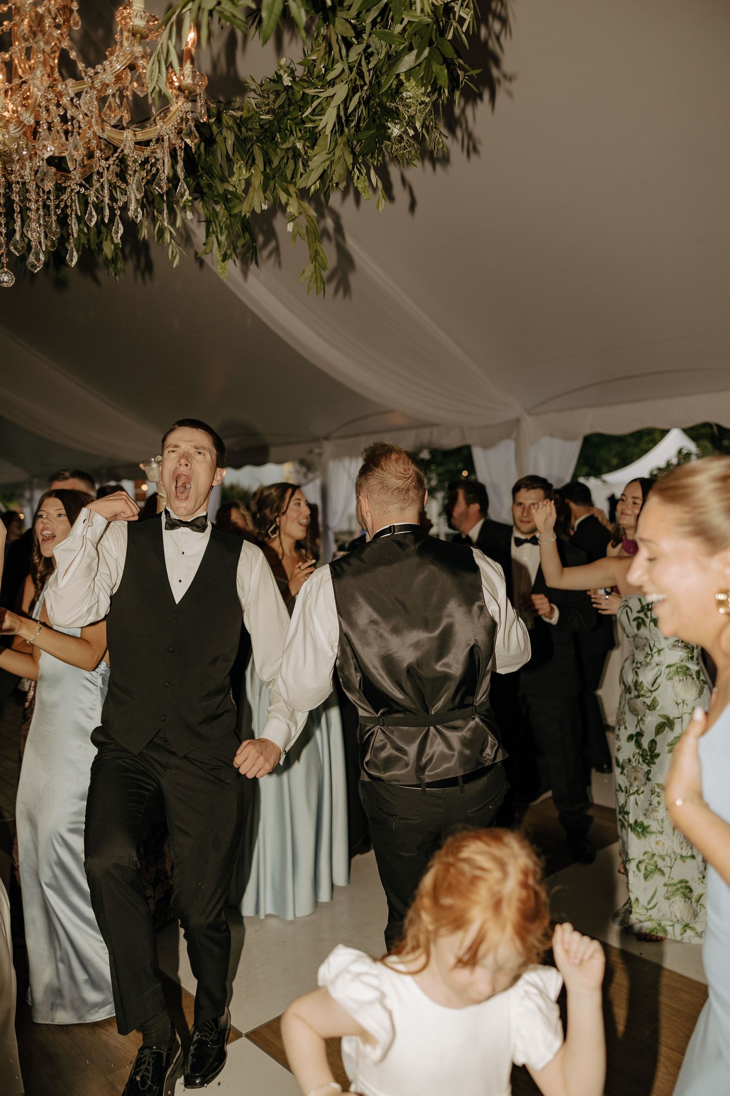 Energetic wedding guest dancing enthusiastically in bow tie at lively tented reception party.