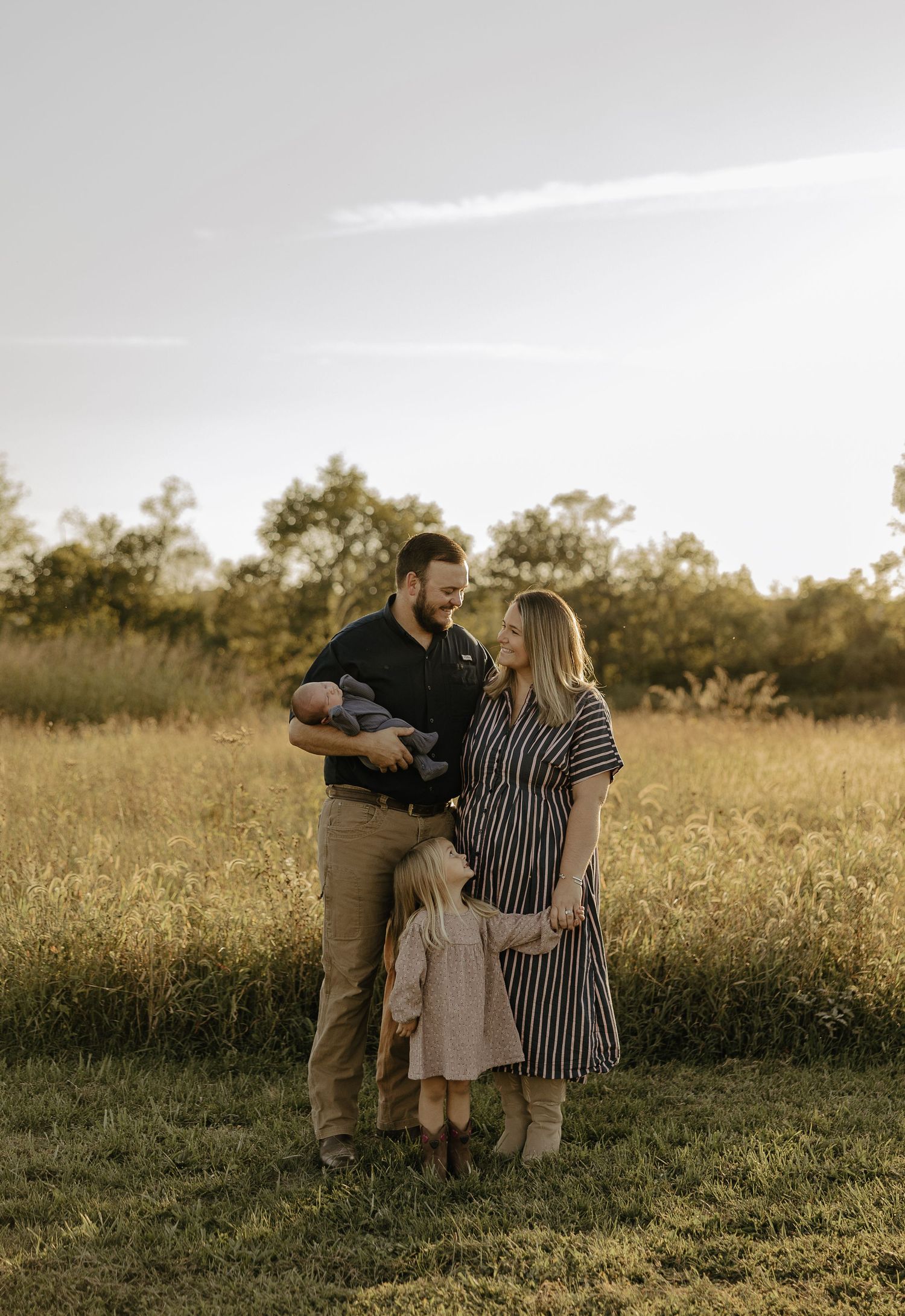 Family sharing tender moments together in a sunlit meadow at sunset.