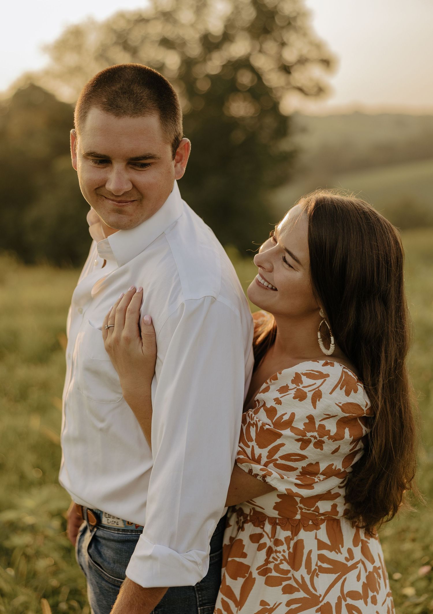 A couple shares an intimate embrace while standing in a sunlit field during golden hour.