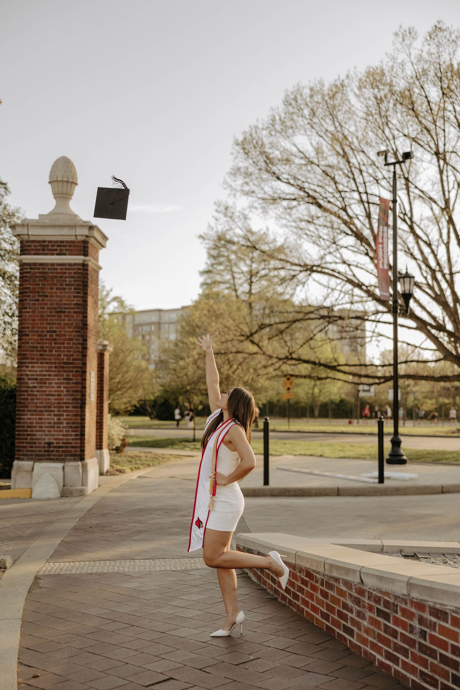 Graduate poses near architectural brick columns during outdoor photo session.