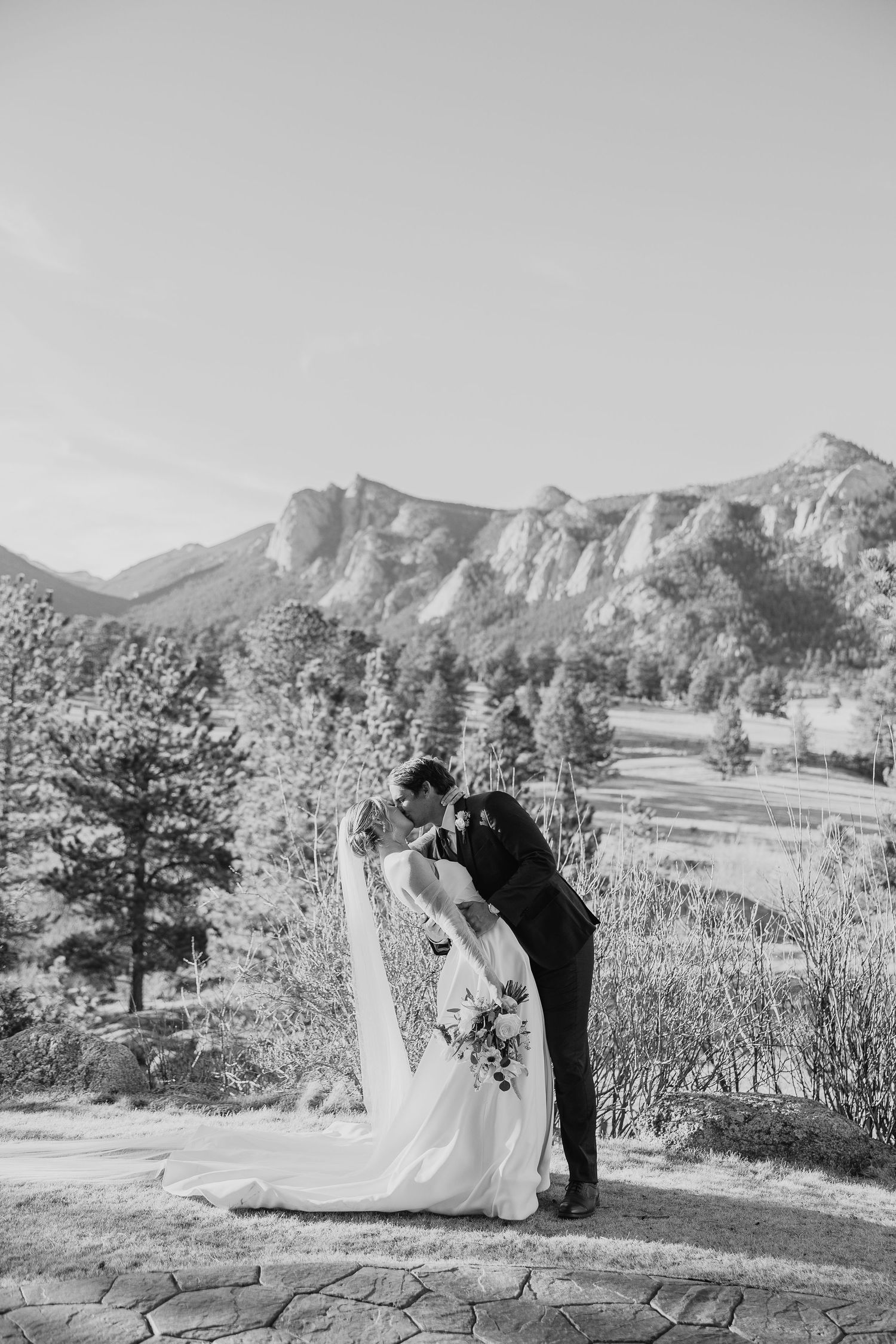 A romantic wedding moment captured in black and white against a backdrop of majestic mountain peaks in Colorado.
