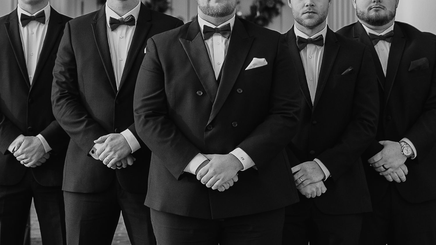 A group of people wearing black tuxedos and bow ties stand in a formal line-up for a portrait.