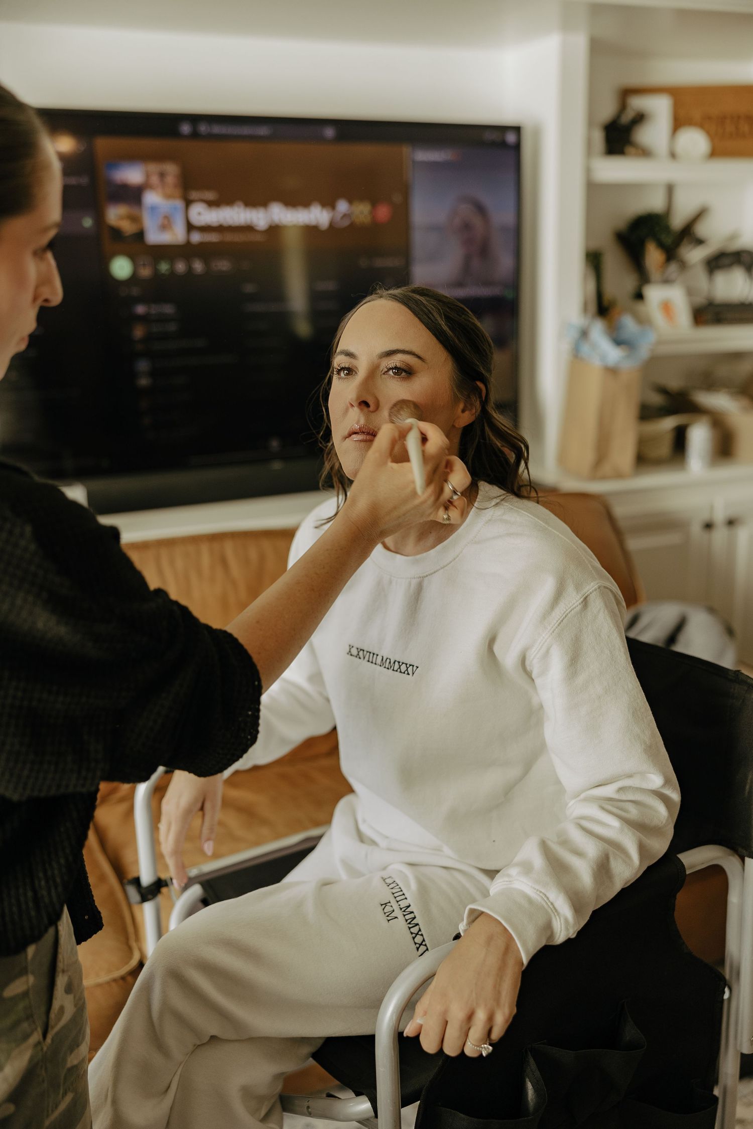Getting makeup professionally applied while wearing a white robe during wedding day preparations.