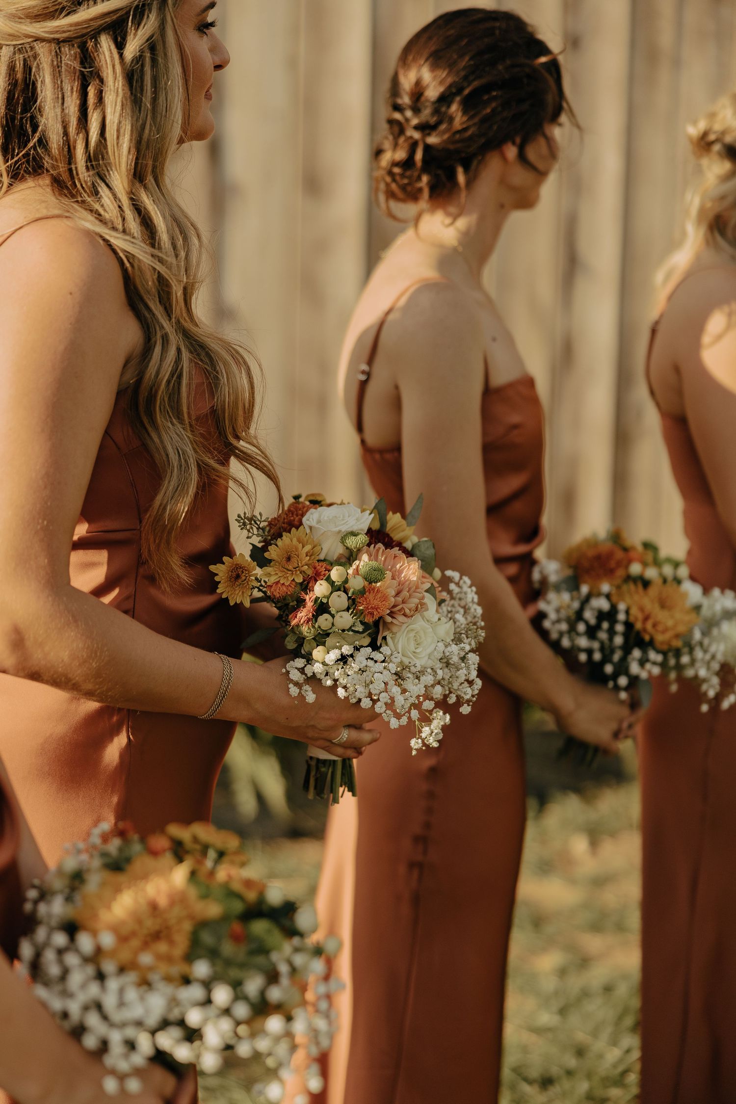 Bridesmaids in terracotta dresses holding rustic floral bouquets.