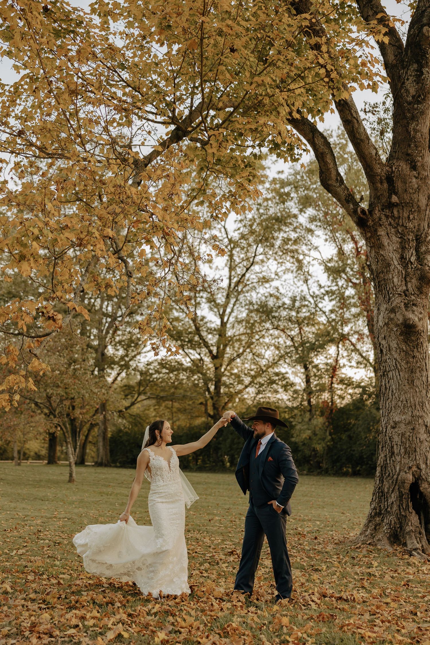 A couple dances among autumn leaves beneath a golden tree.