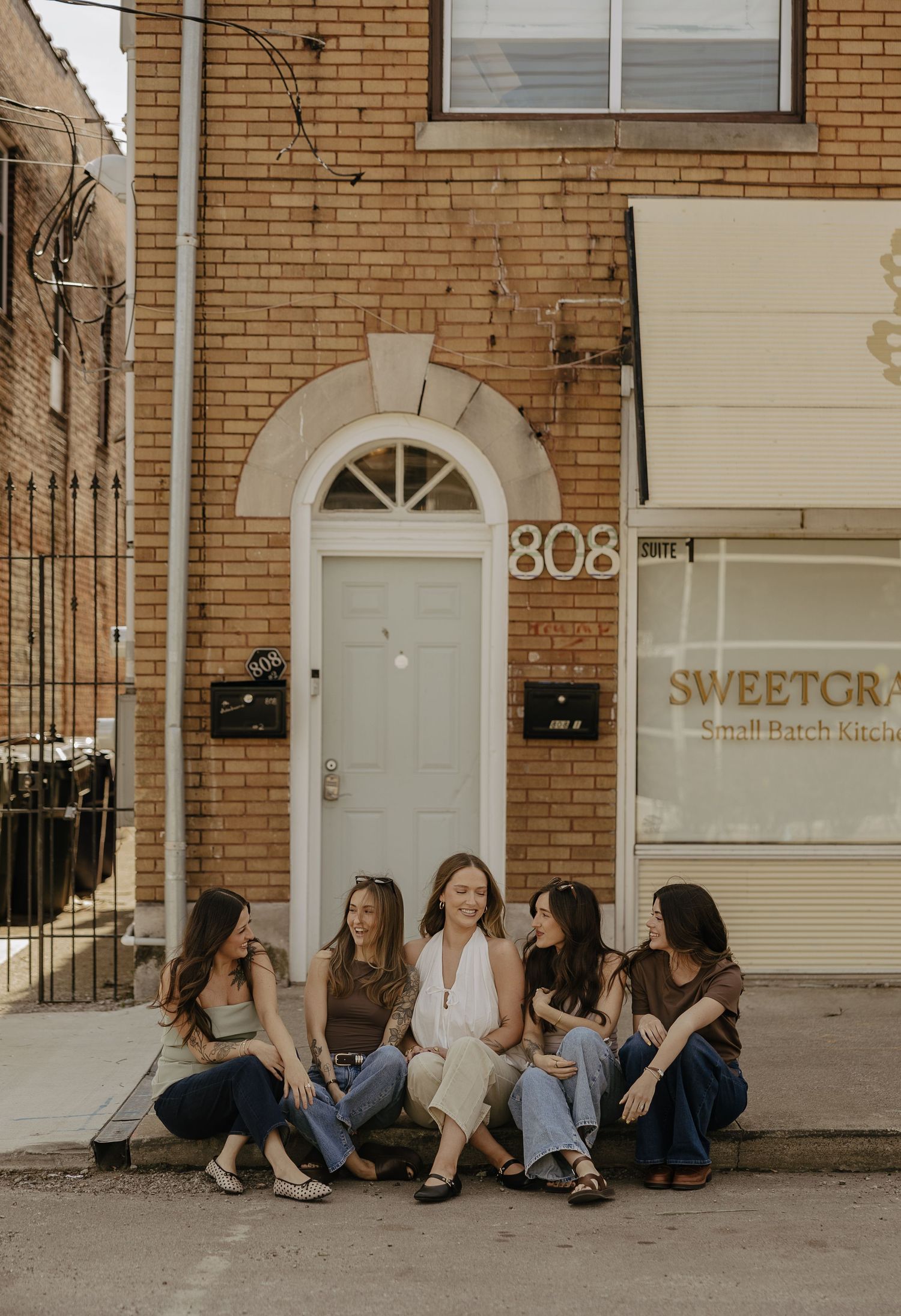 Five women sit together outside a brick building at 808, next to Sweetgrass Small Batch Kitchen.