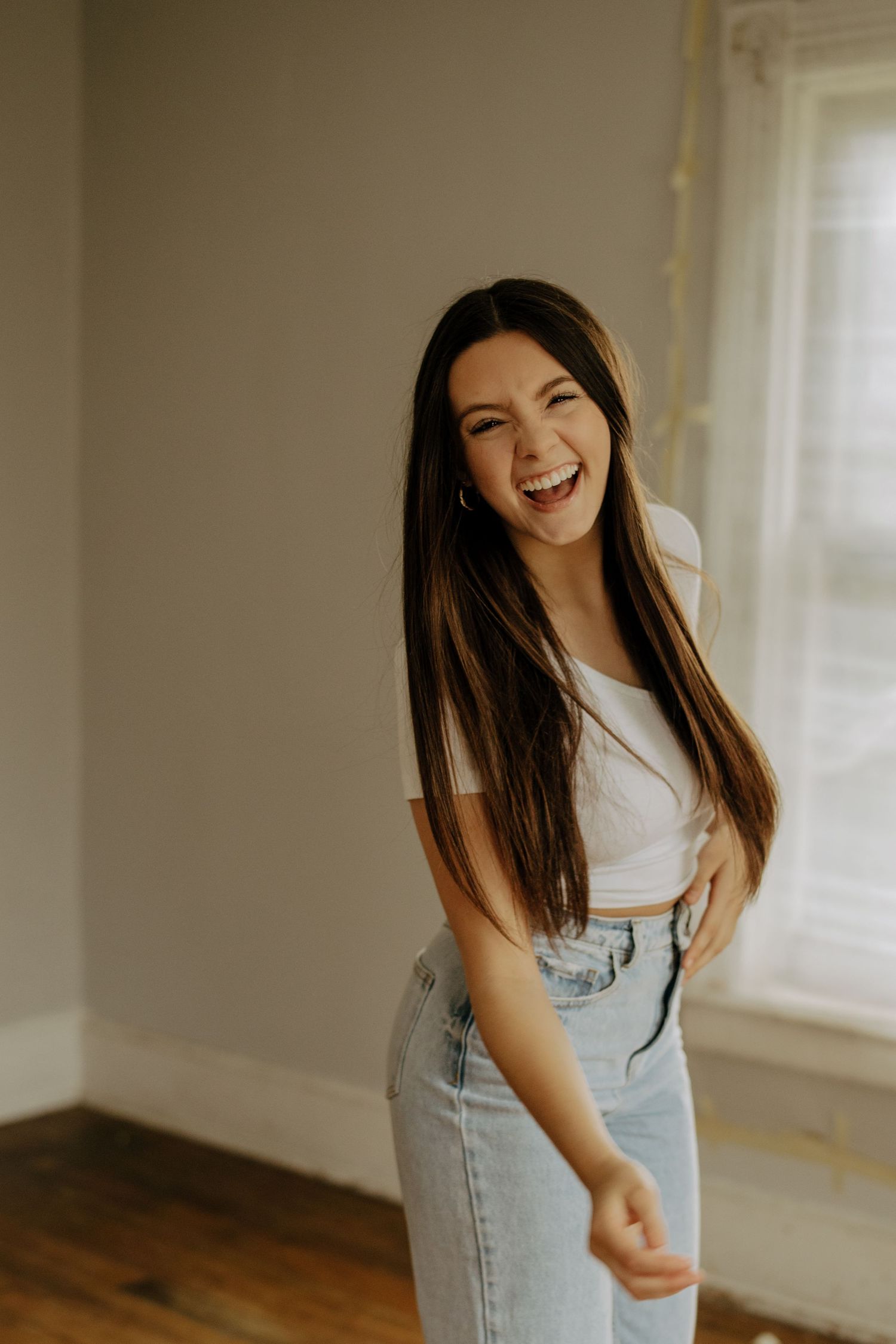 A person in a white top and light denim jeans dances joyfully in a bright sunlit room.