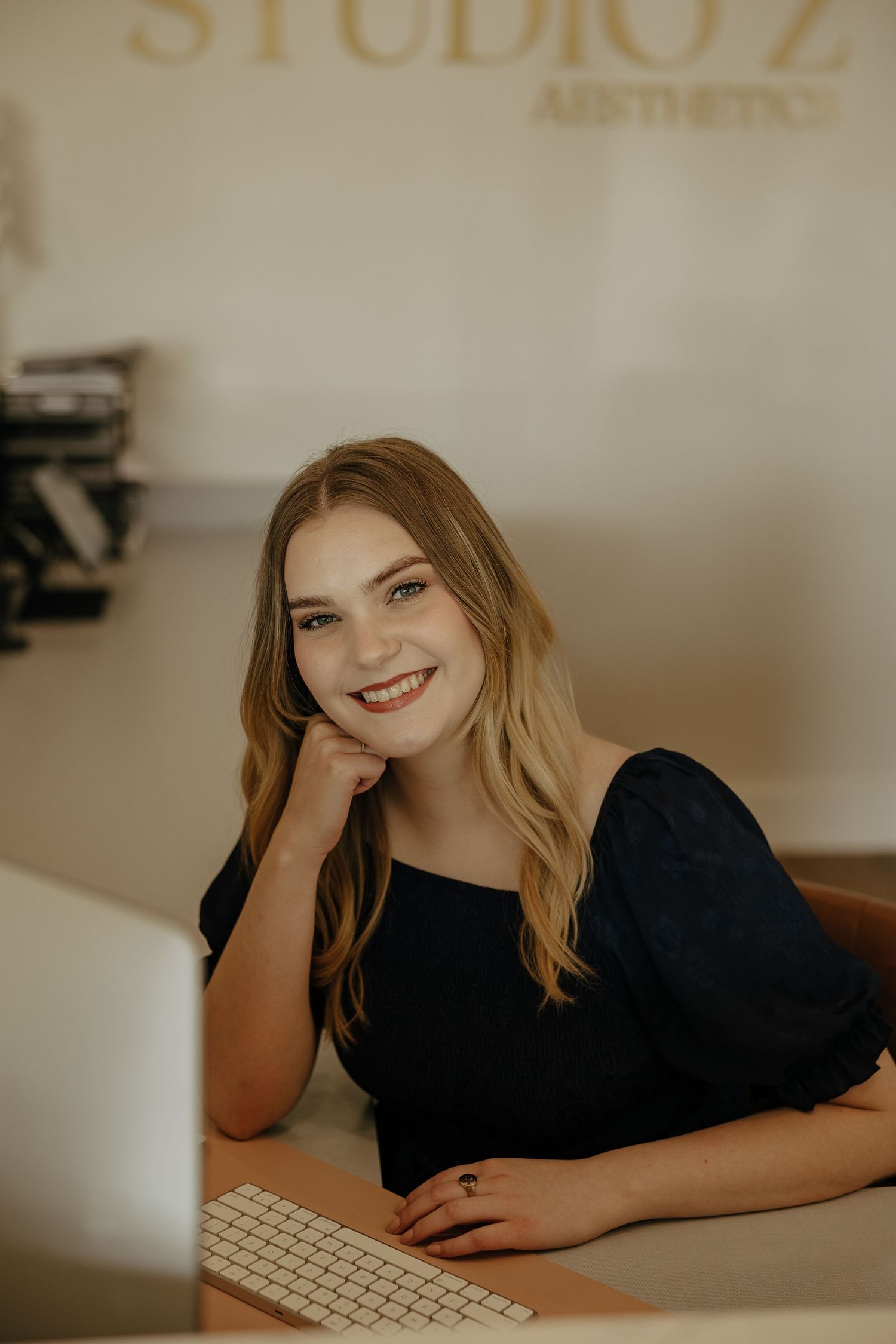 Casual workplace portrait at a desk with computer showing natural warm lighting and professional attire.