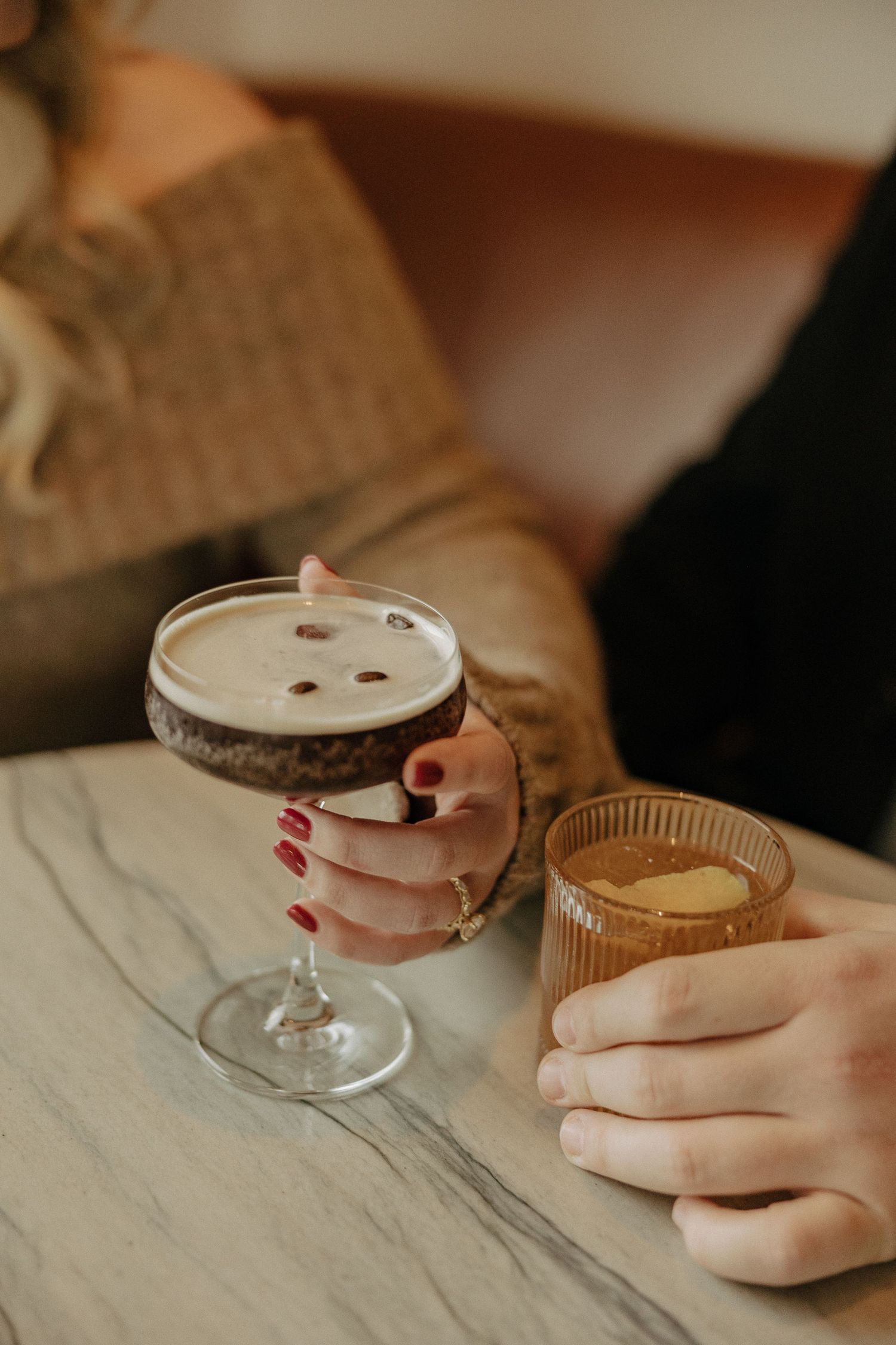 A delicate cocktail glass with pink liquid sits on a marble surface in moody lighting.