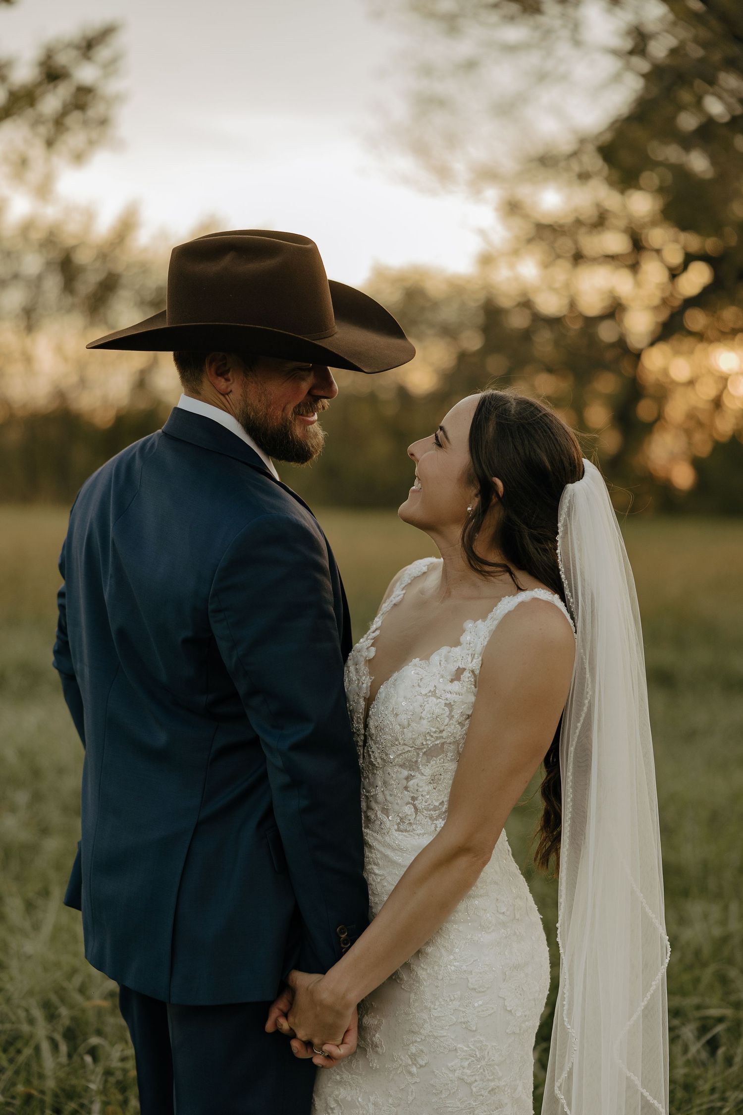 A romantic wedding couple embraces during golden hour in a rustic outdoor setting.