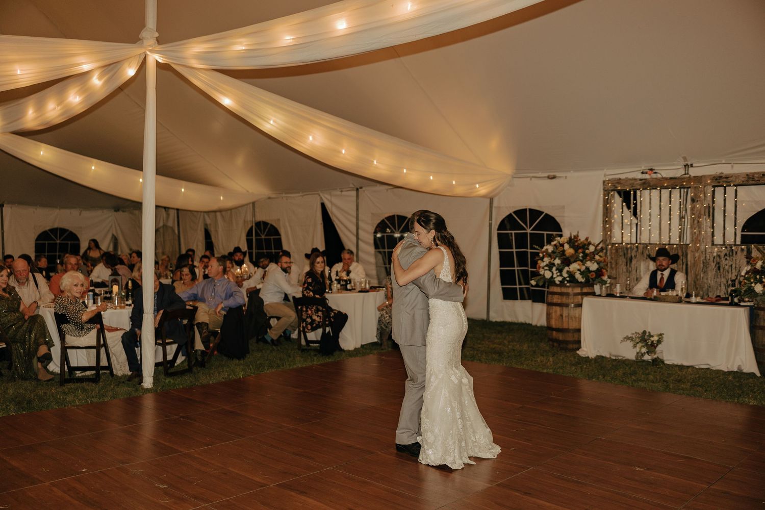 Wedding reception under white tent with string lights and wooden dance floor.
