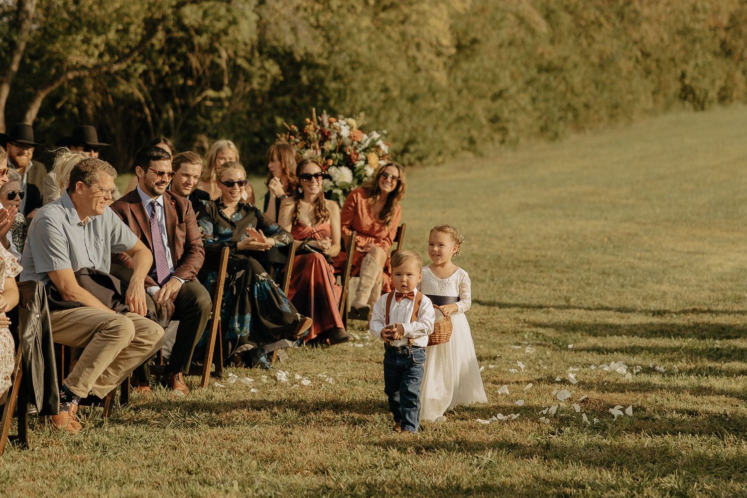 Wedding ceremony guests seated on wooden chairs on a grassy hillside.