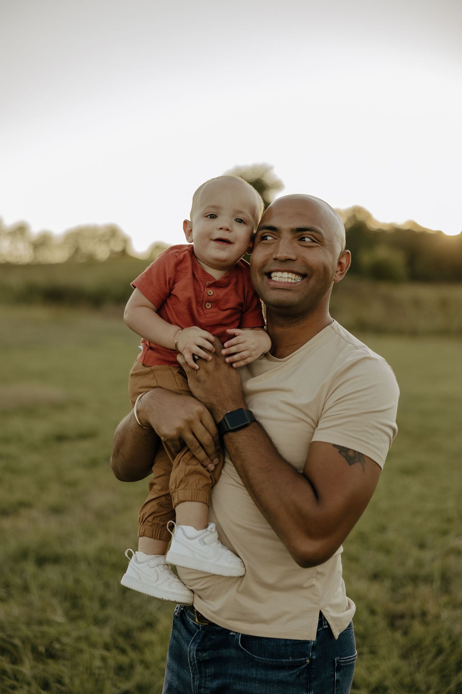 Father and baby share joyful moments together in outdoor field at sunset.