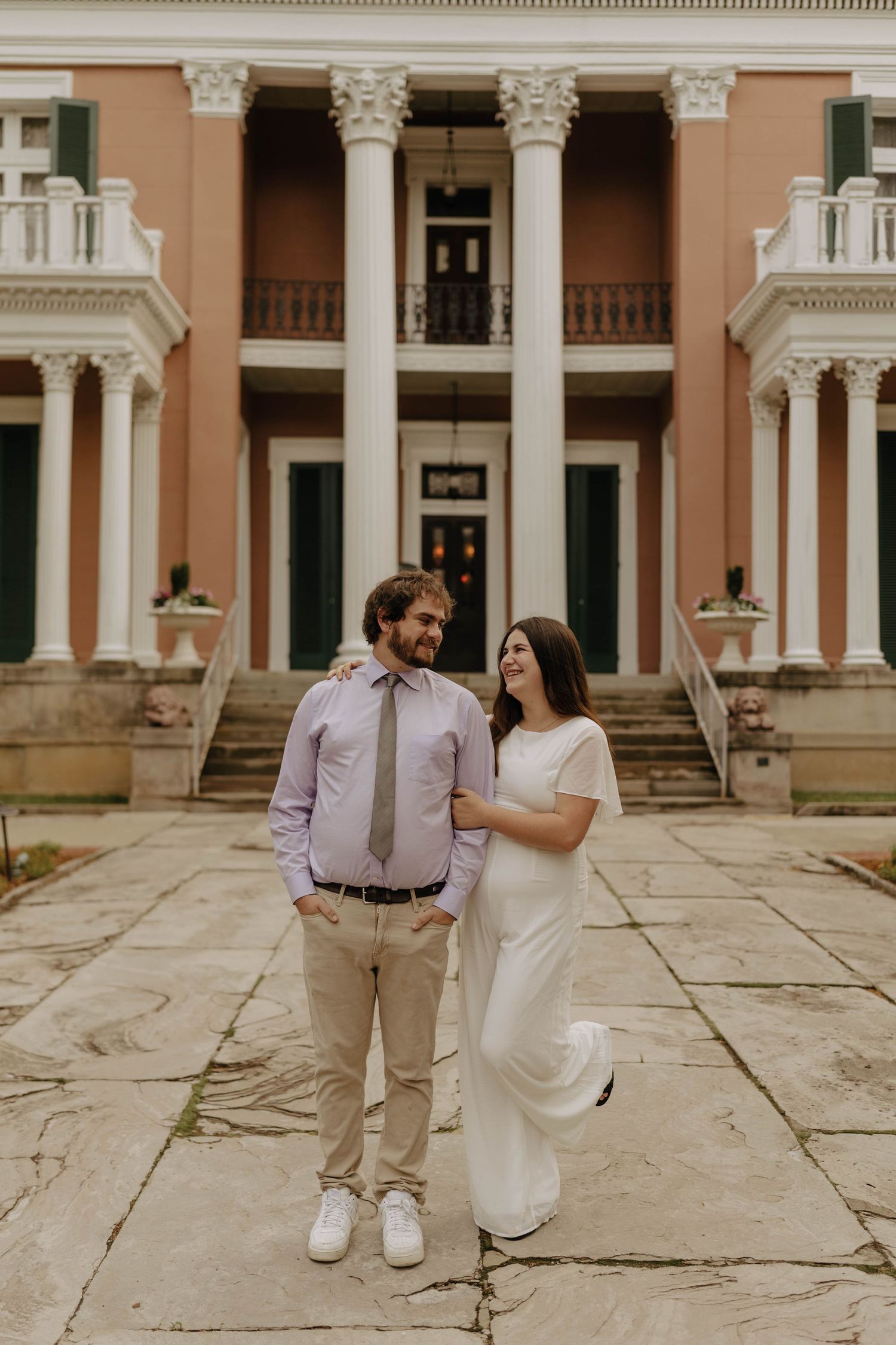 A couple dances playfully on stone pavers in front of a historic building with columns.