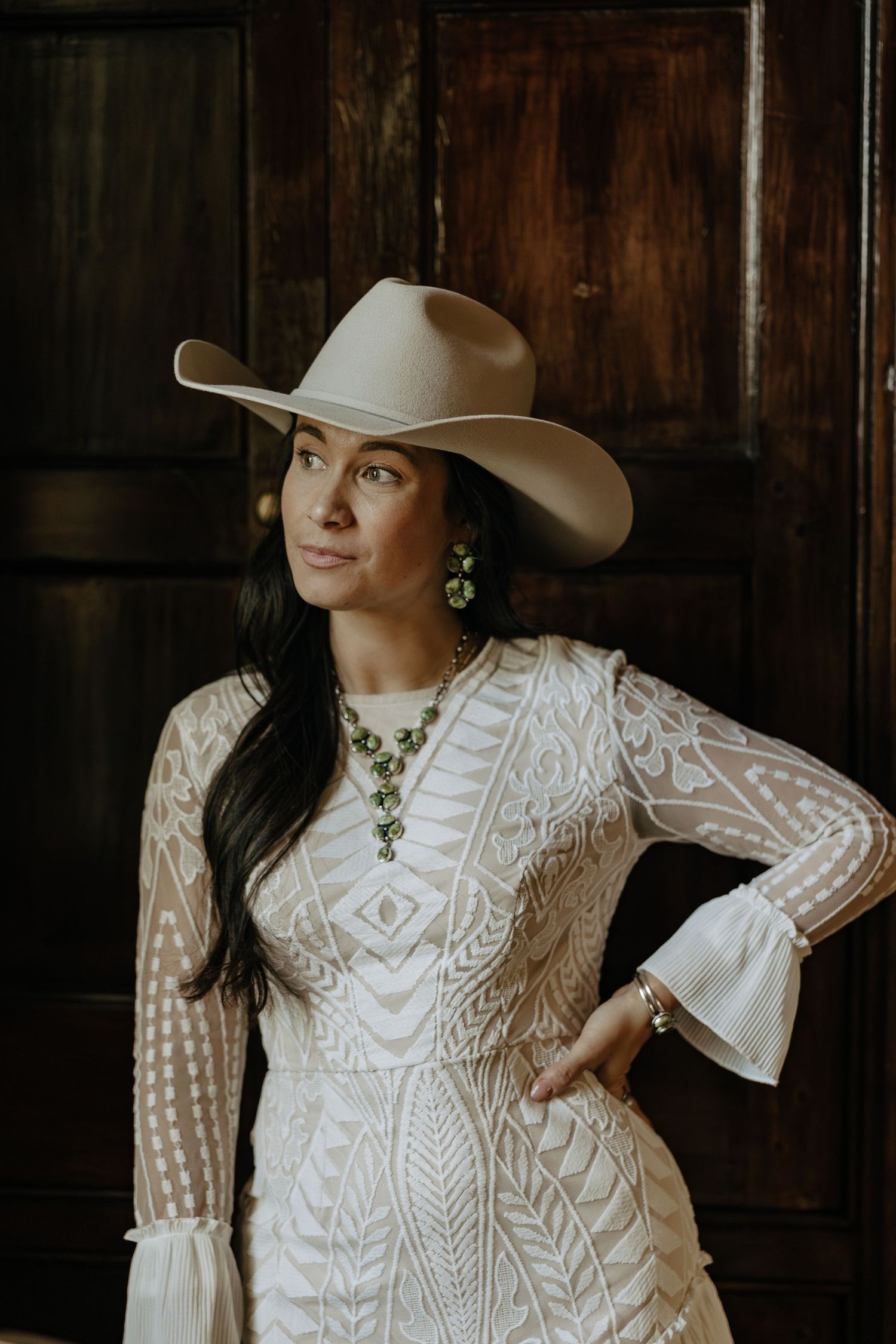 A white lace dress with intricate patterns and a wide-brimmed hat create a Western-inspired look.