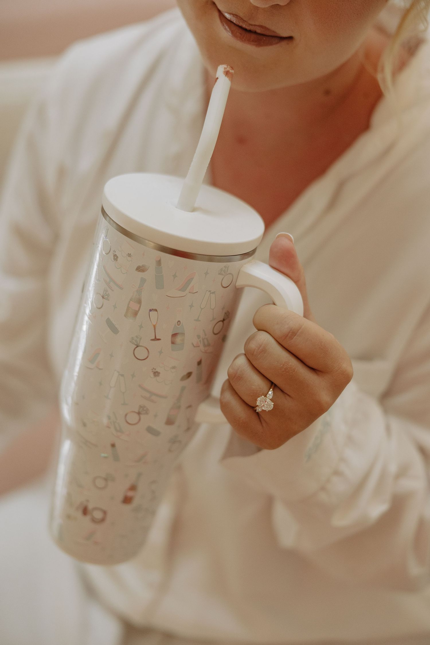 Someone holds a decorative coffee cup with a white shirt and ring visible.
