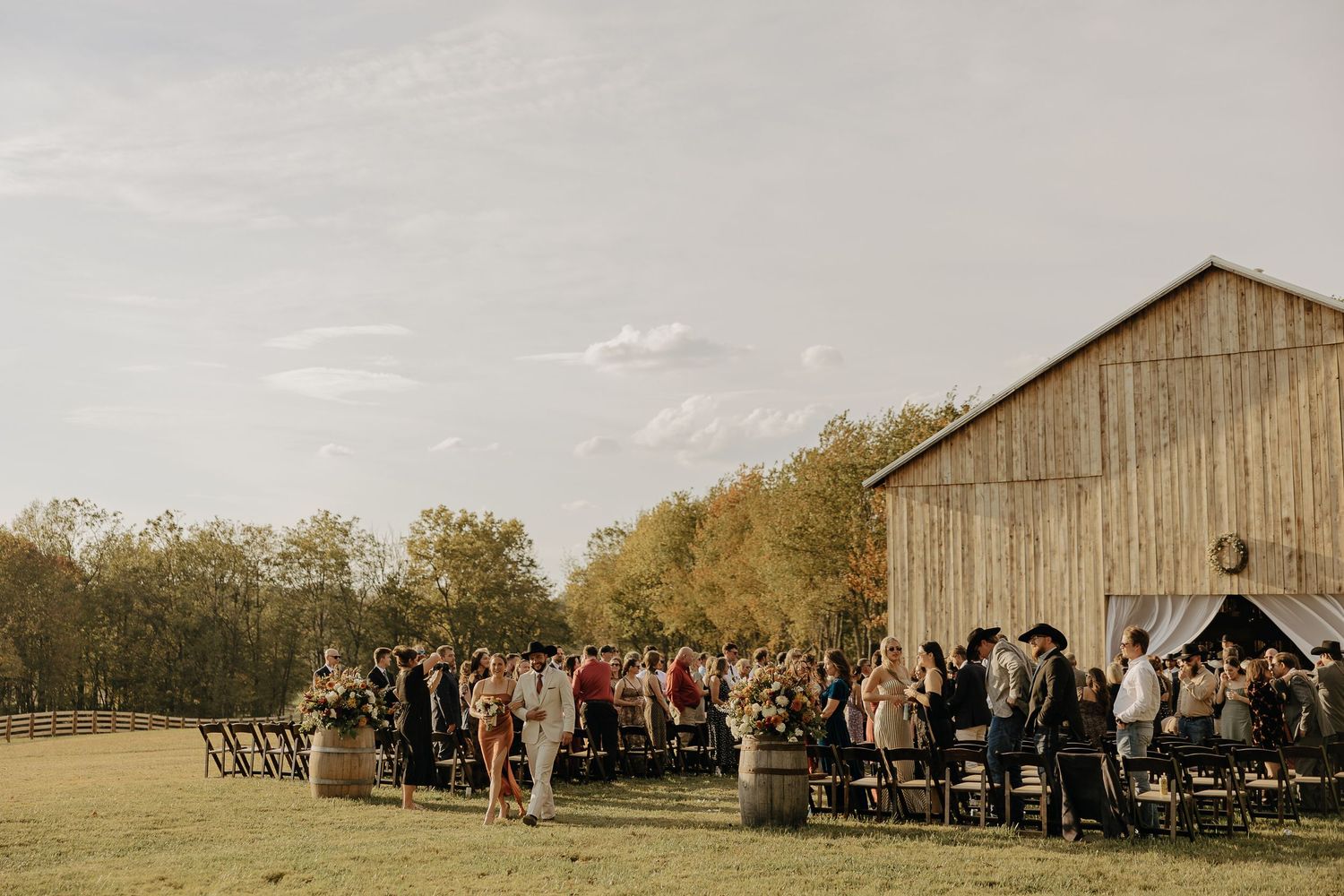 Wide shot of wooden barn with wedding guests gathered for outdoor ceremony.