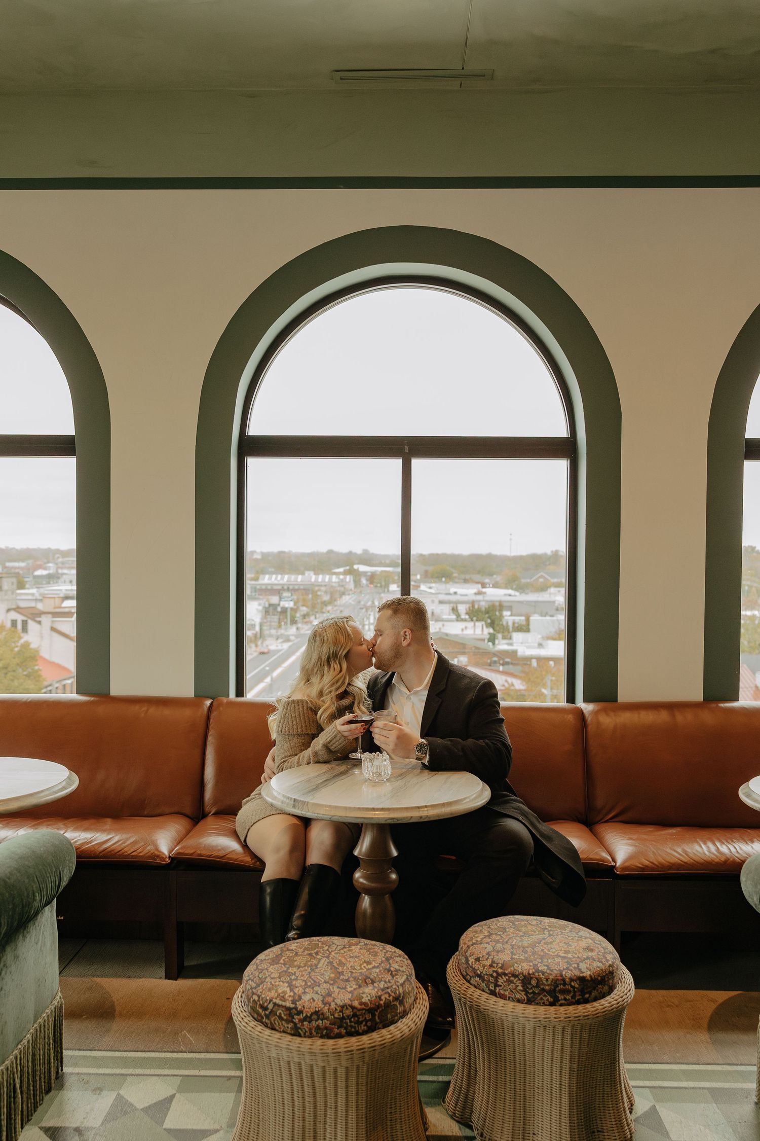 A couple sits at a table by arched windows overlooking a scenic cityscape view.