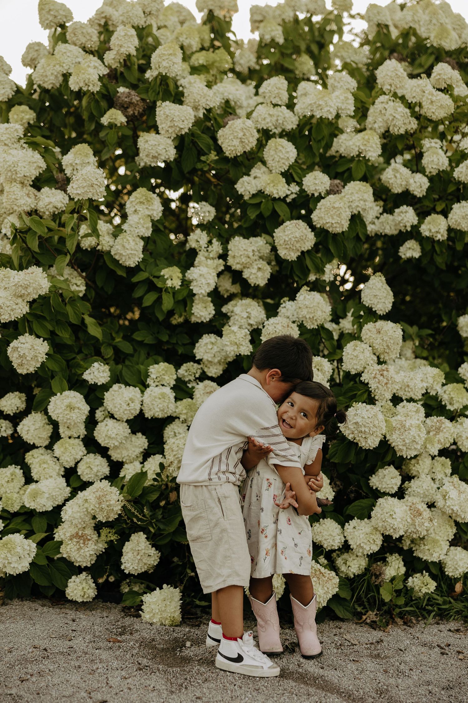 White hydrangea bushes frame a sweet moment in matching white outfits.