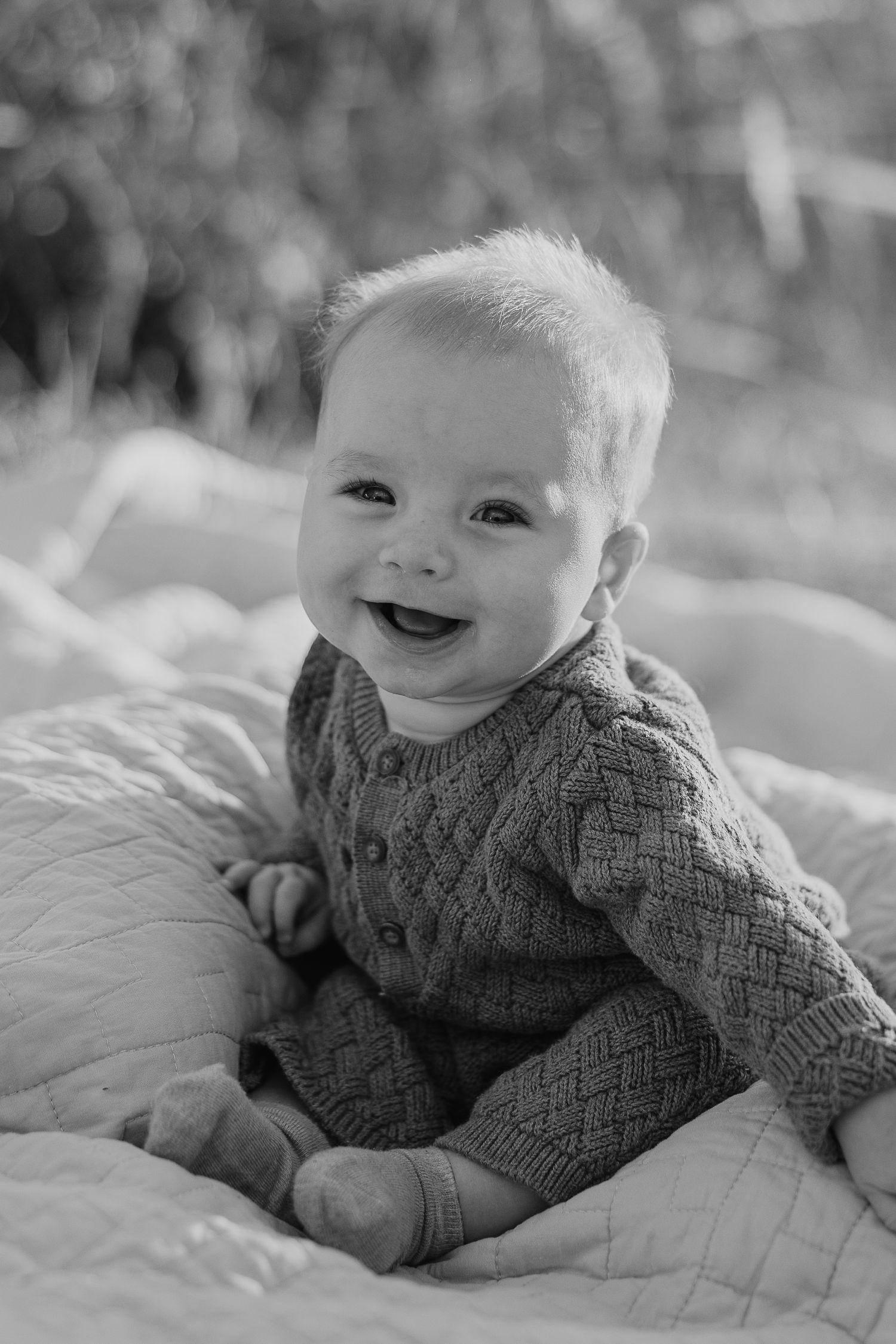 Black and white portrait series of baby smiling on white blanket.