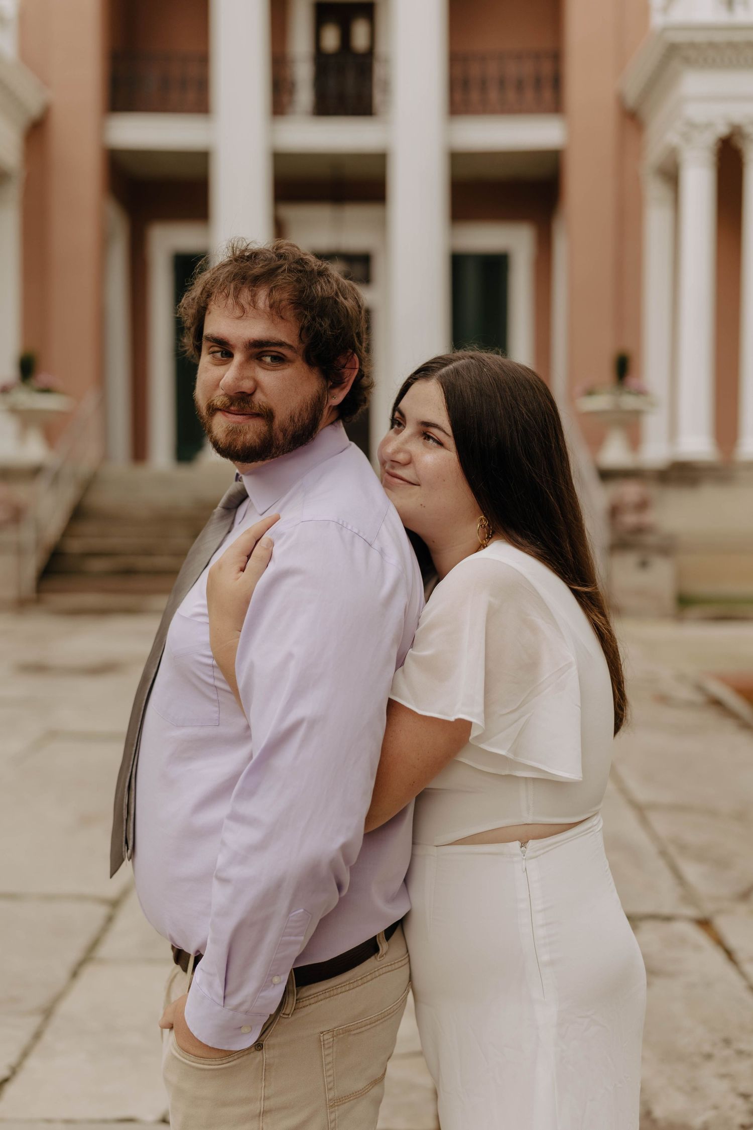 A couple embraces intimately in front of a peach-colored neoclassical building.
