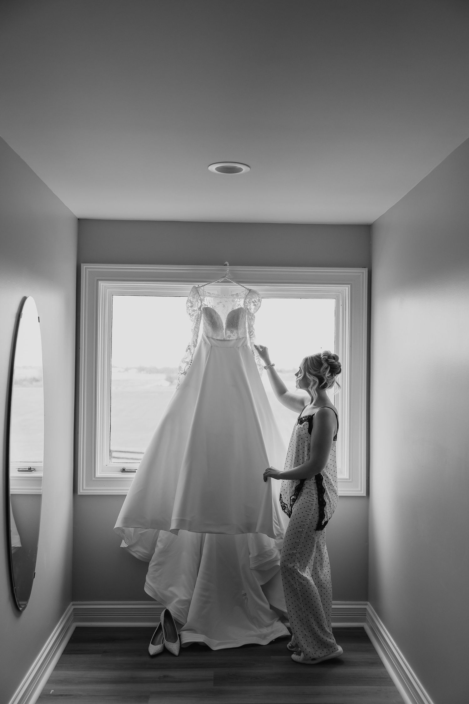 Wedding dress hanging in preparation before the ceremony in a minimalist white room.