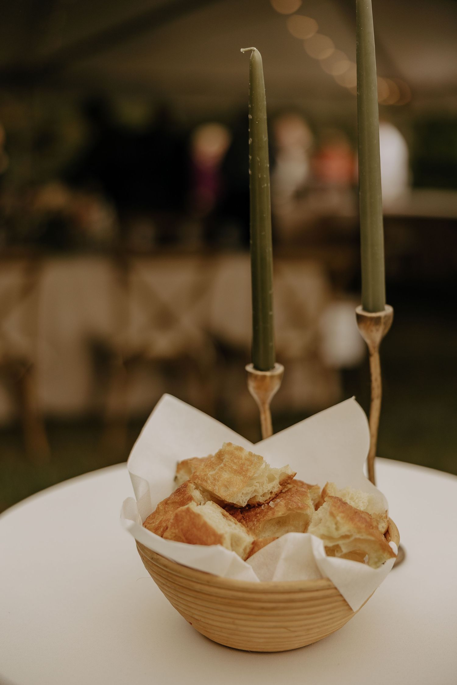 Elegant table setting with tall green candles and bread baskets at a wedding reception.