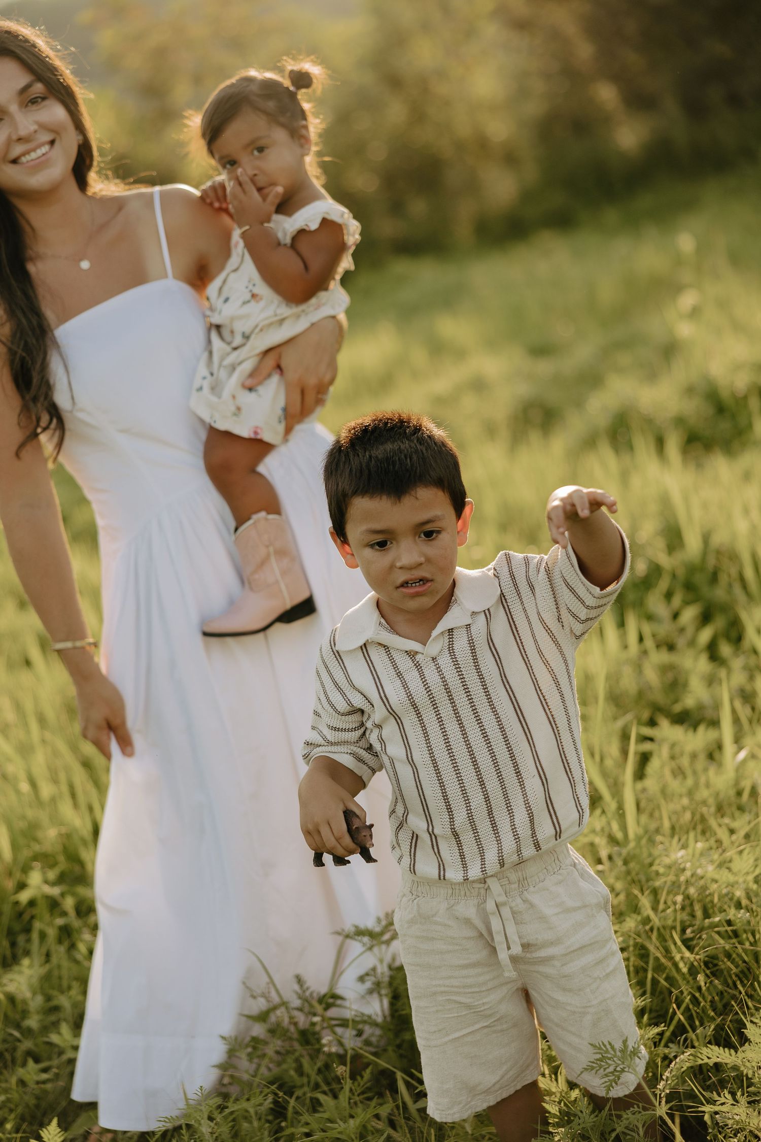 Family enjoying playful moments together in a sunlit grassy field during golden hour.