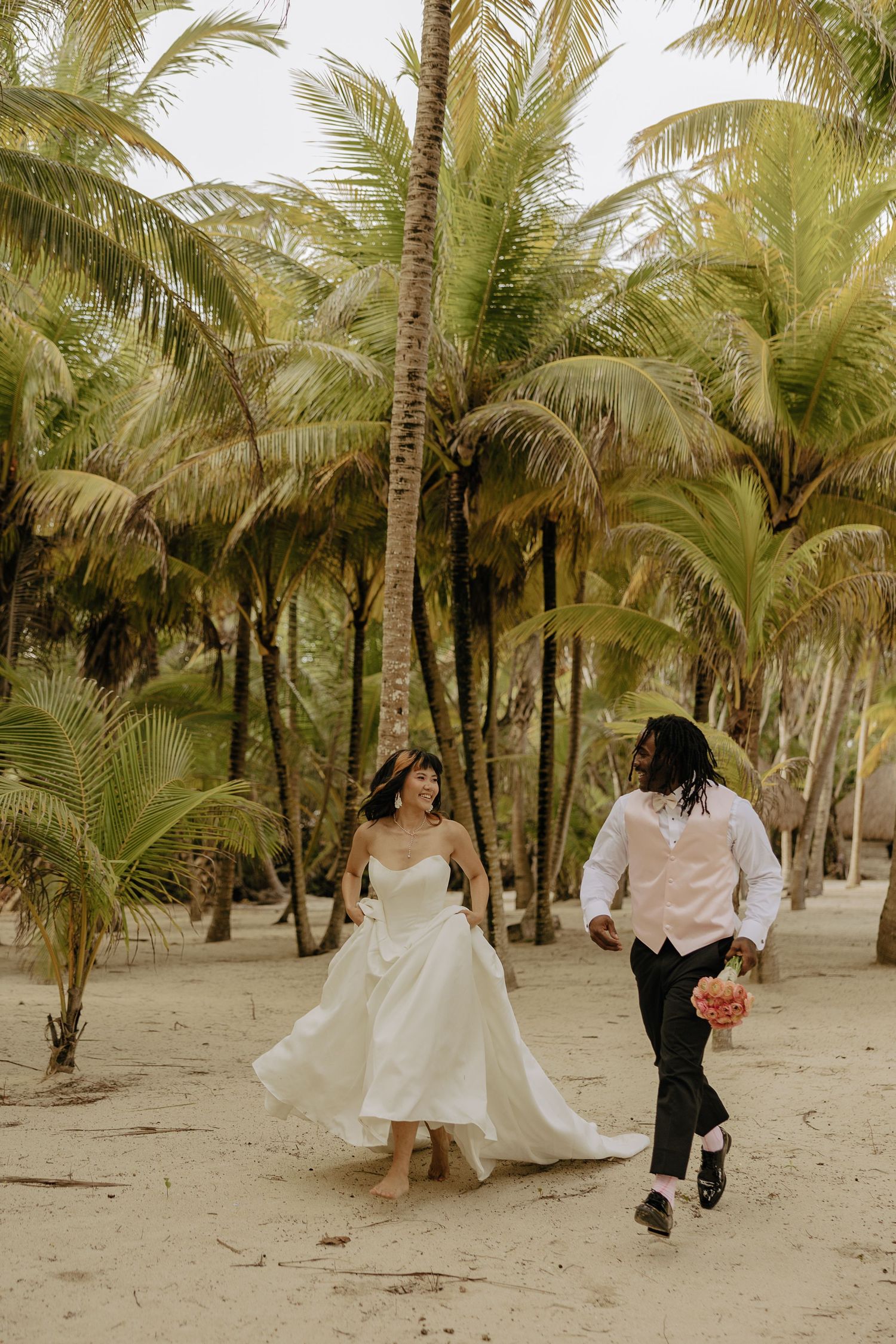A romantic wedding photoshoot among palm trees on a sandy beach with flowing white dress and natural lighting.