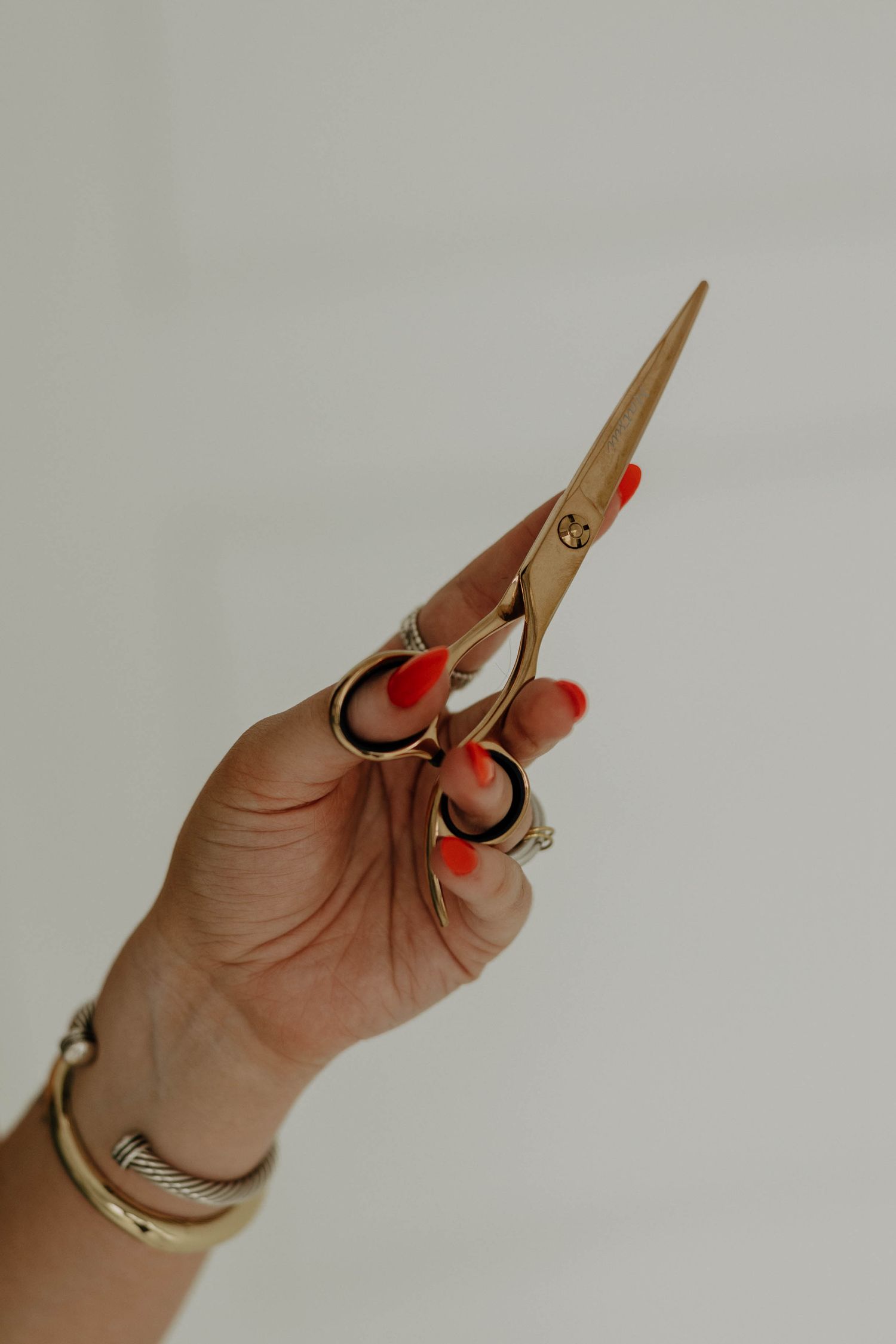 A hand with red nail polish holds up gold-toned scissors against a white background.