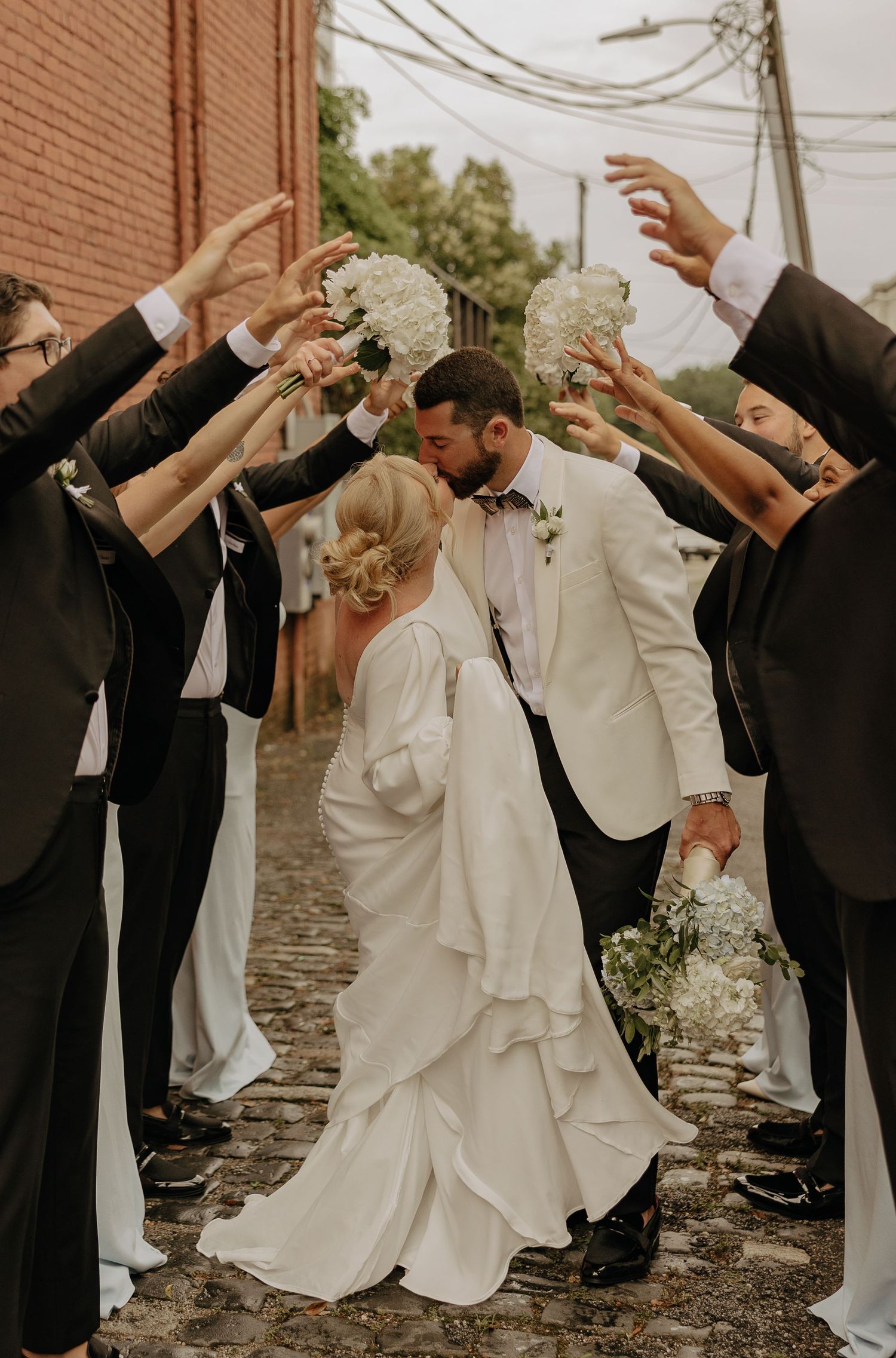 Wedding party performs a fun dance move on a stone path with the couple in white and black attire.