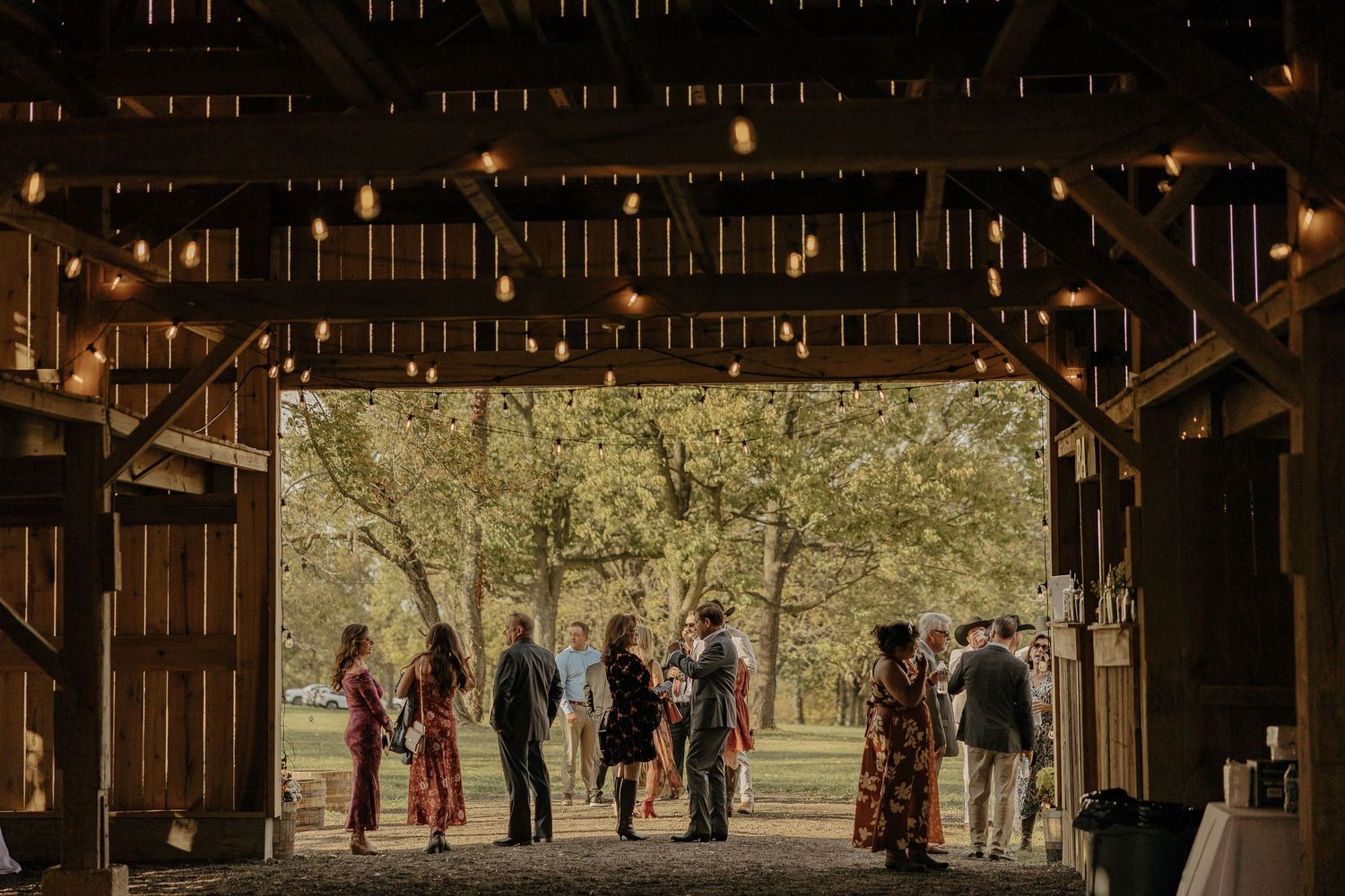 Wedding guests gathered inside a rustic barn venue with natural lighting streaming through.