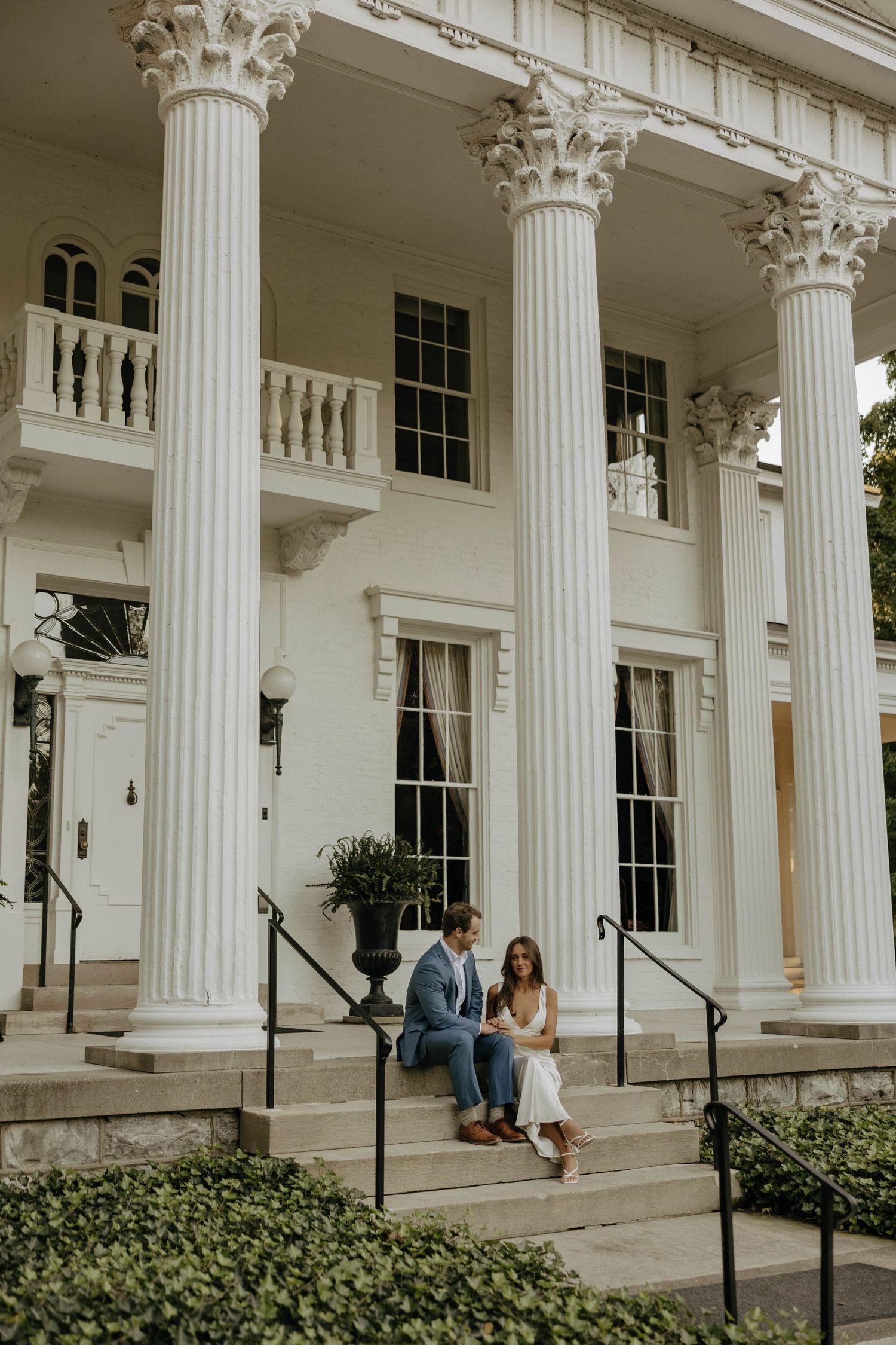 Elegant white colonial building with tall columns serves as backdrop for romantic photoshoot.