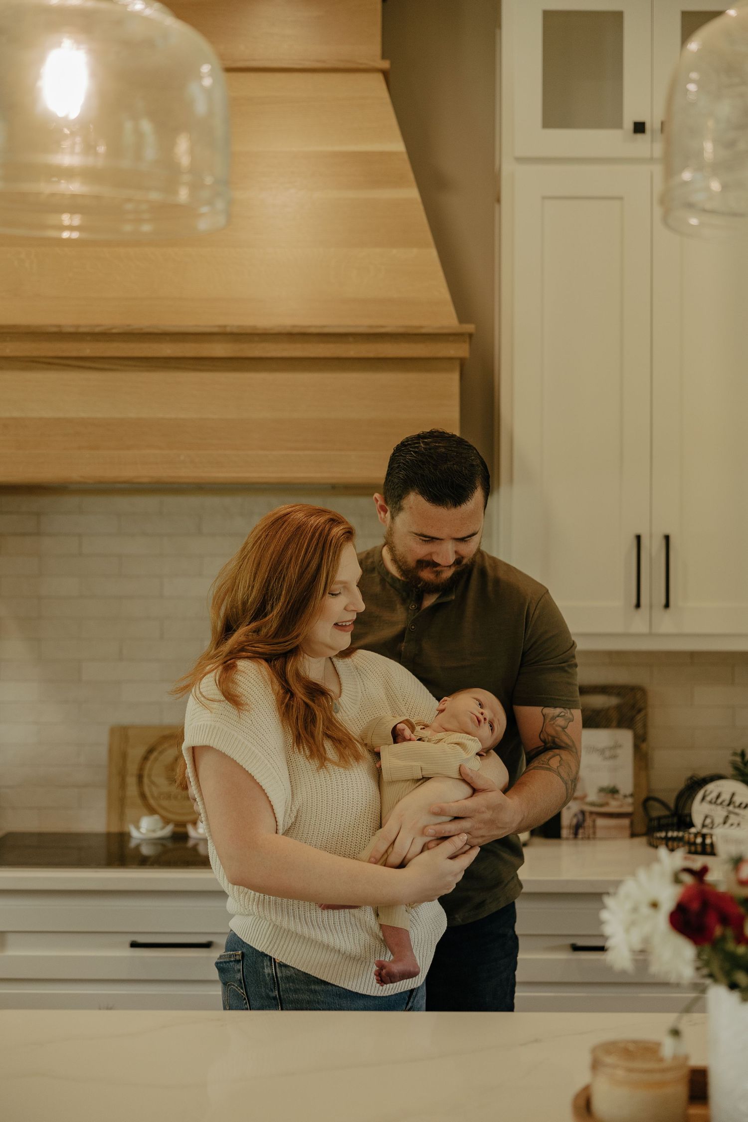 A tender family moment in a modern kitchen as parents cradle their newborn baby.