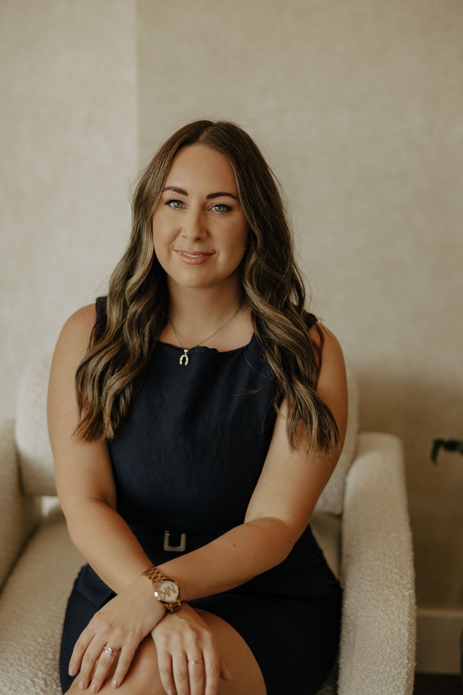 Professional headshot in black dress against neutral background with modern aesthetic.